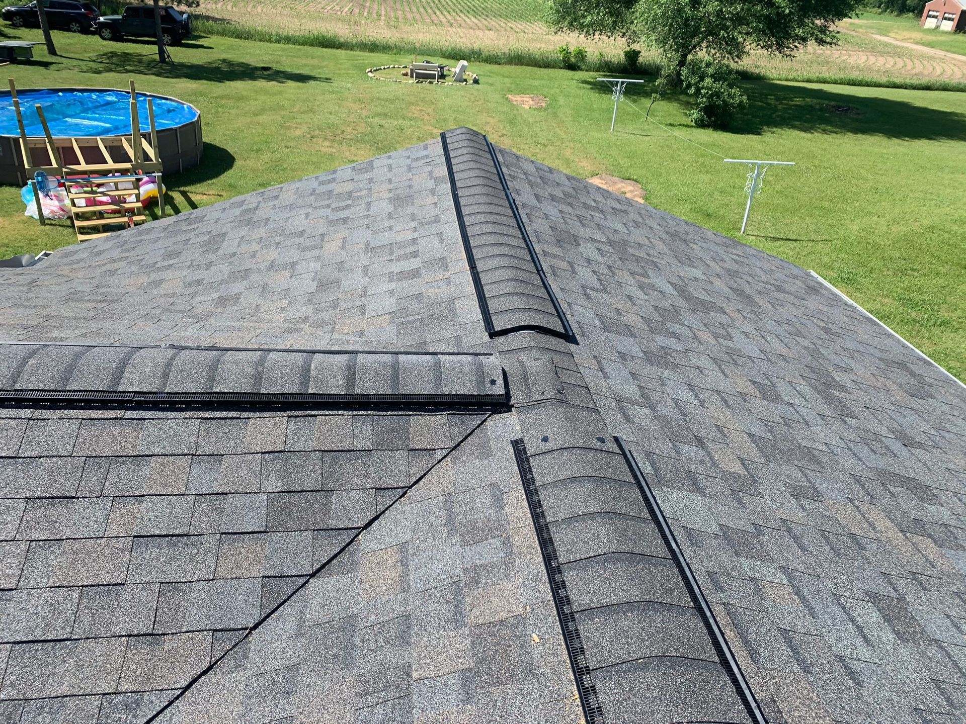 Gray shingled roof with dark ridge vents, viewed from above with a grassy yard and trampoline in the background