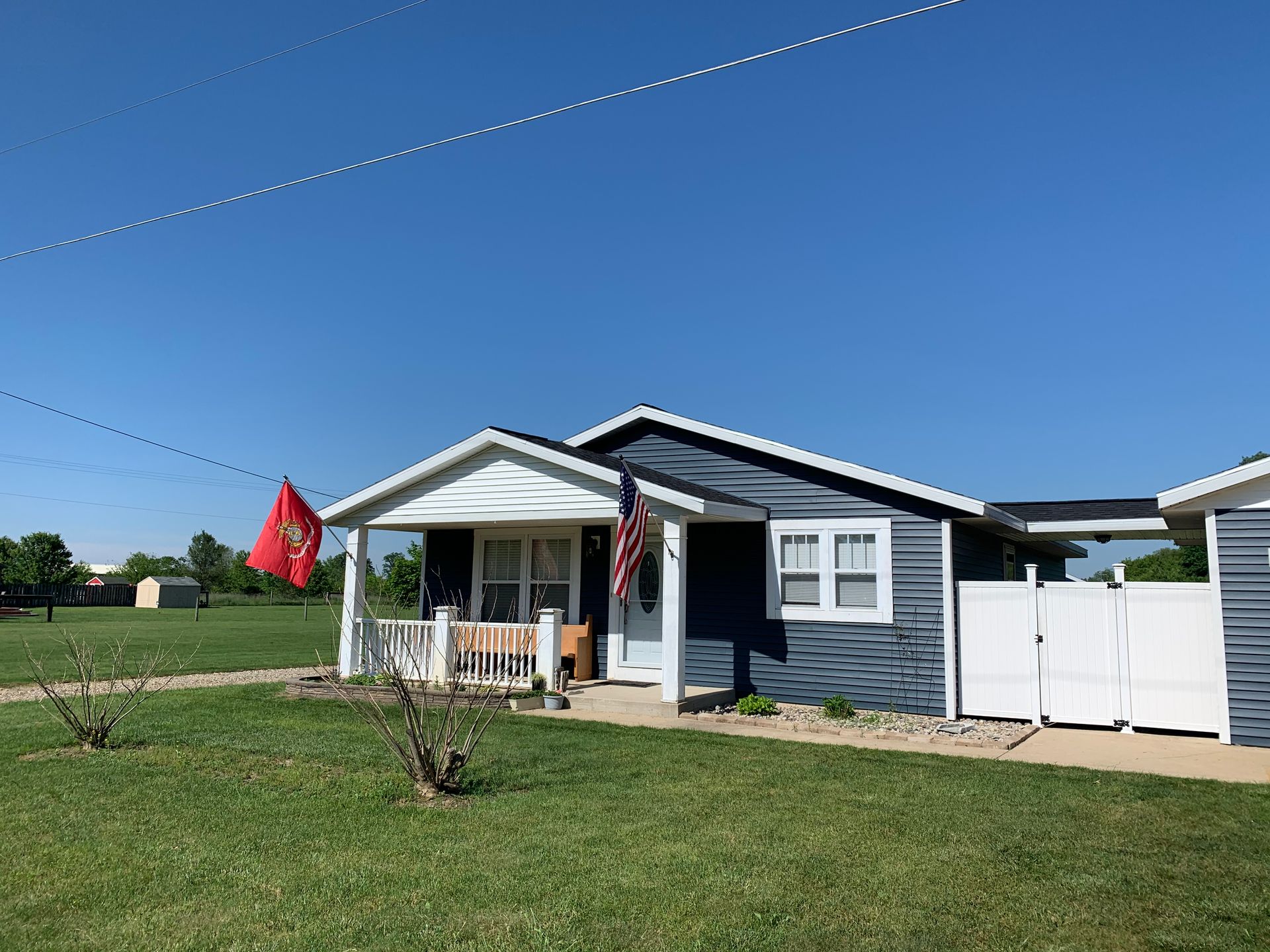 Small blue house with a white porch and red flag on a sunny lawn