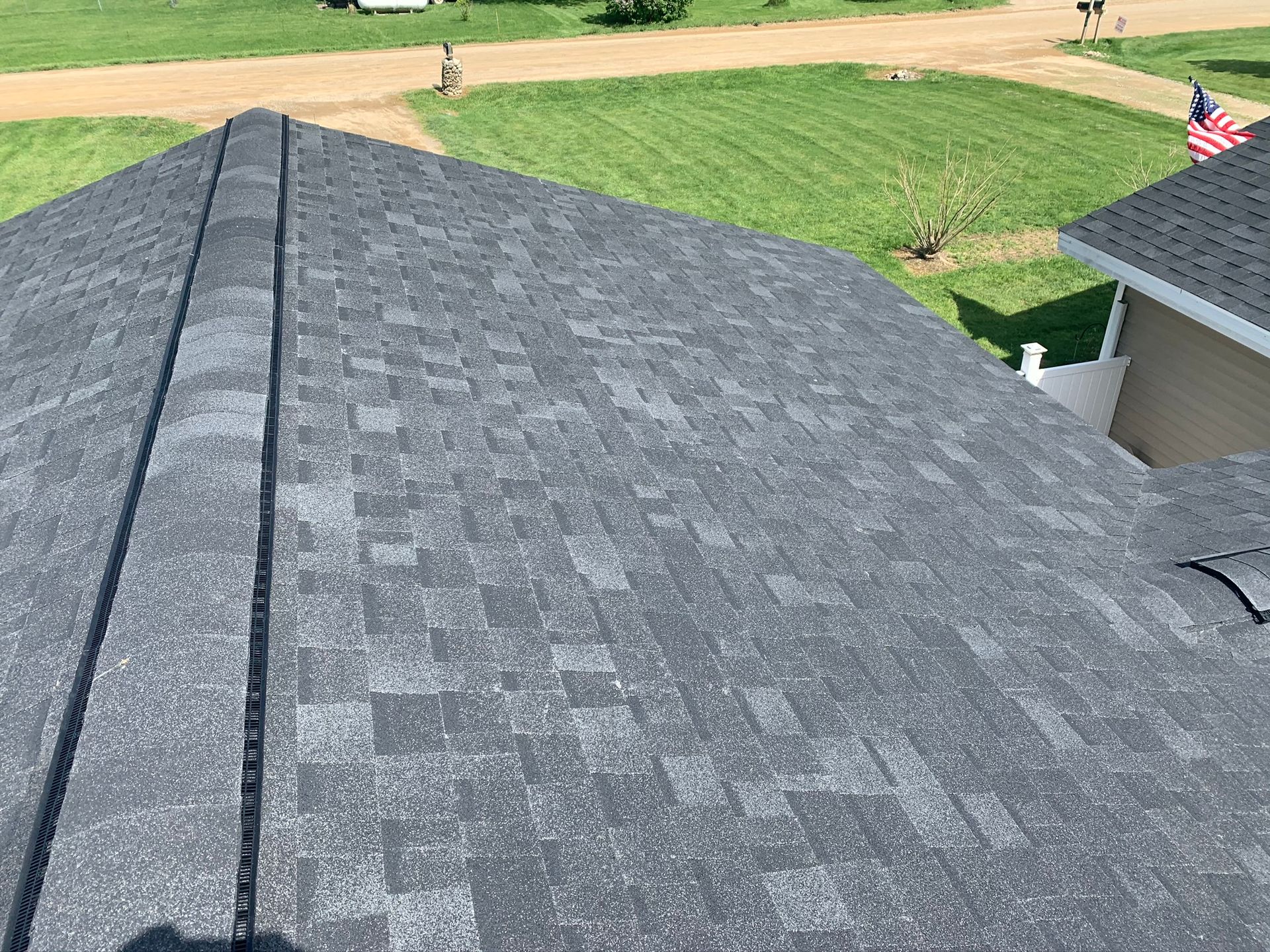 Gray shingle roof with a valley seam, viewed from above beside a lawn and driveway