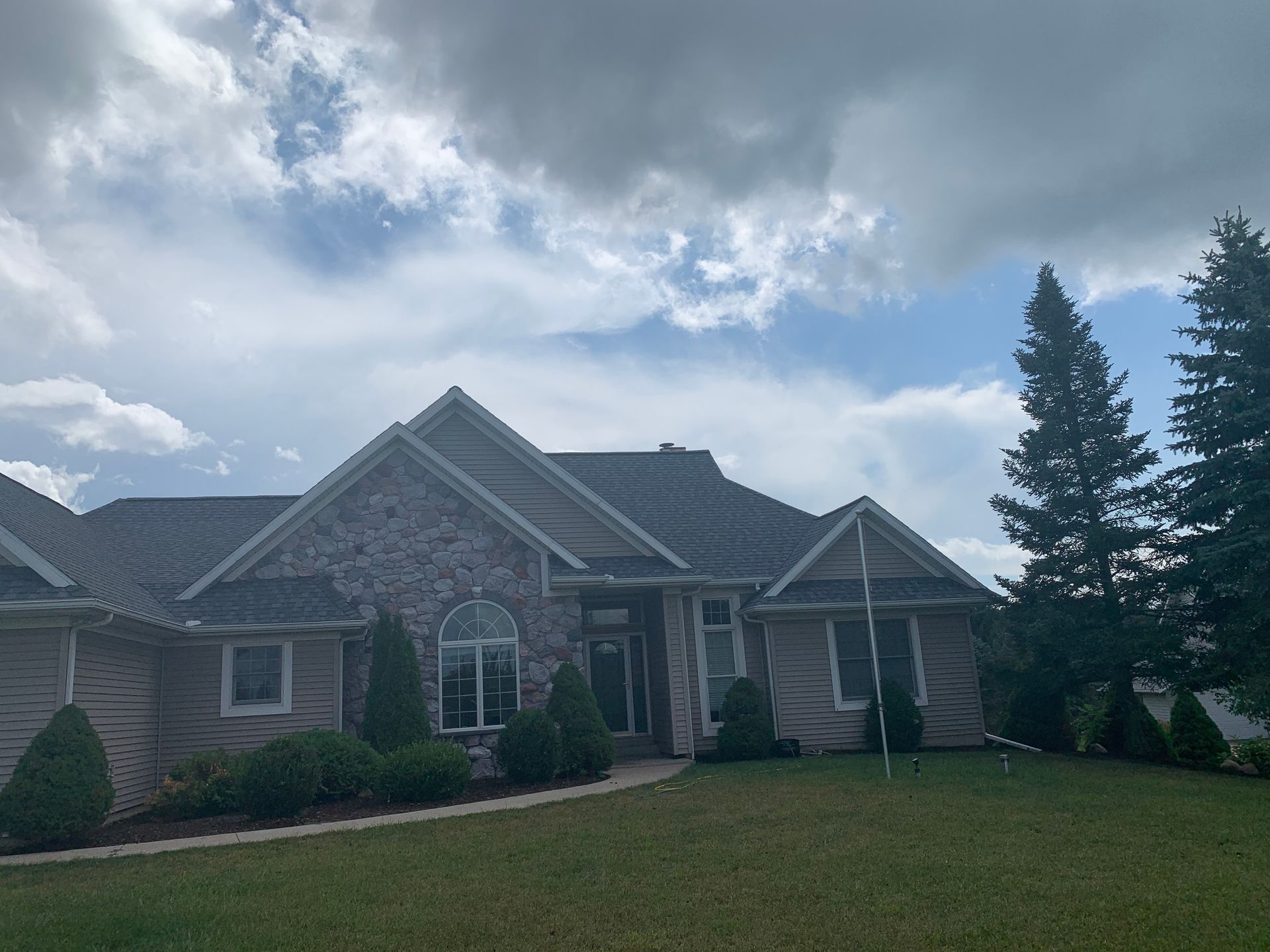 Suburban brick house with a gabled roof, front lawn, and cloudy sky above