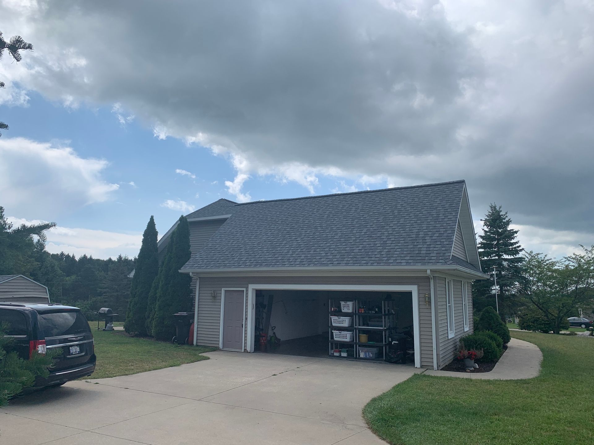 Detached garage with open door, parked SUV, and cloudy sky over a suburban driveway