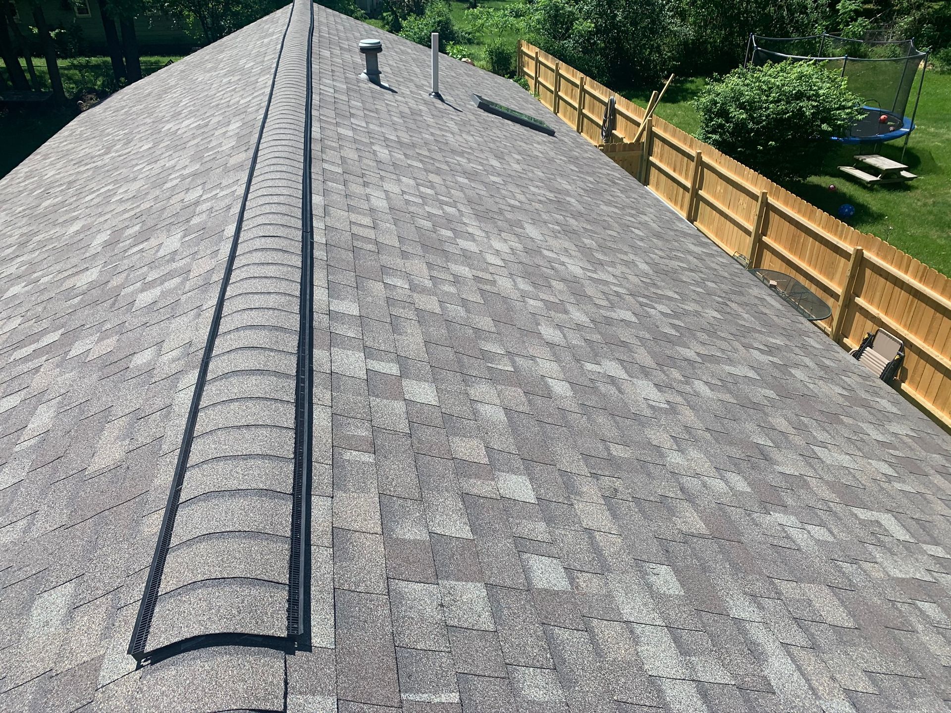 Rooftop with gray shingles, a central vent ridge, and a wooden fence along the edge.