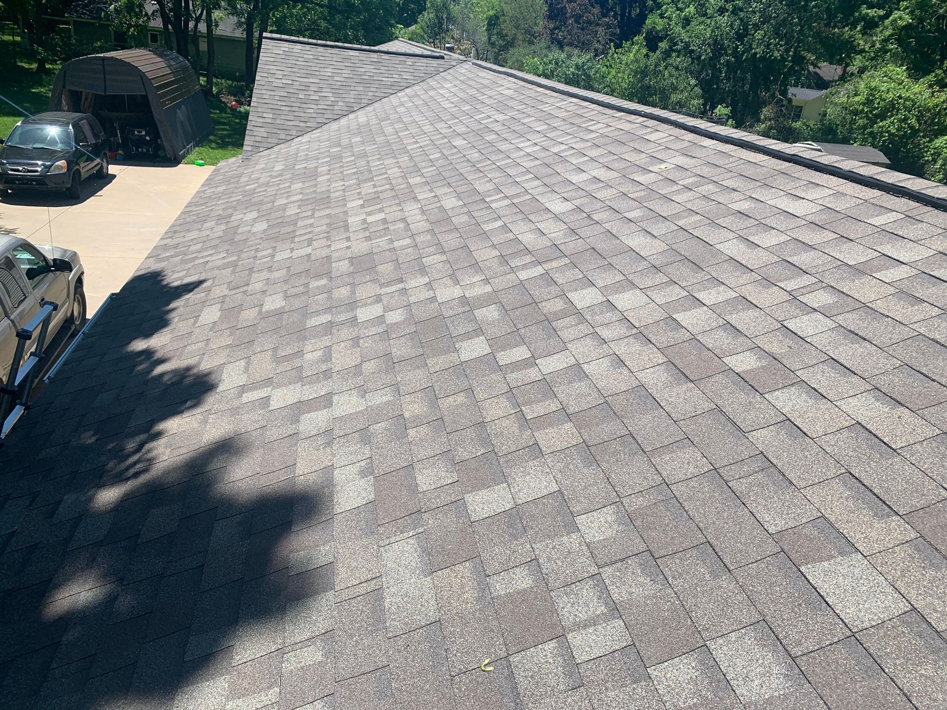 Roof covered in gray shingles, viewed from above with trees and parked cars along the edge.