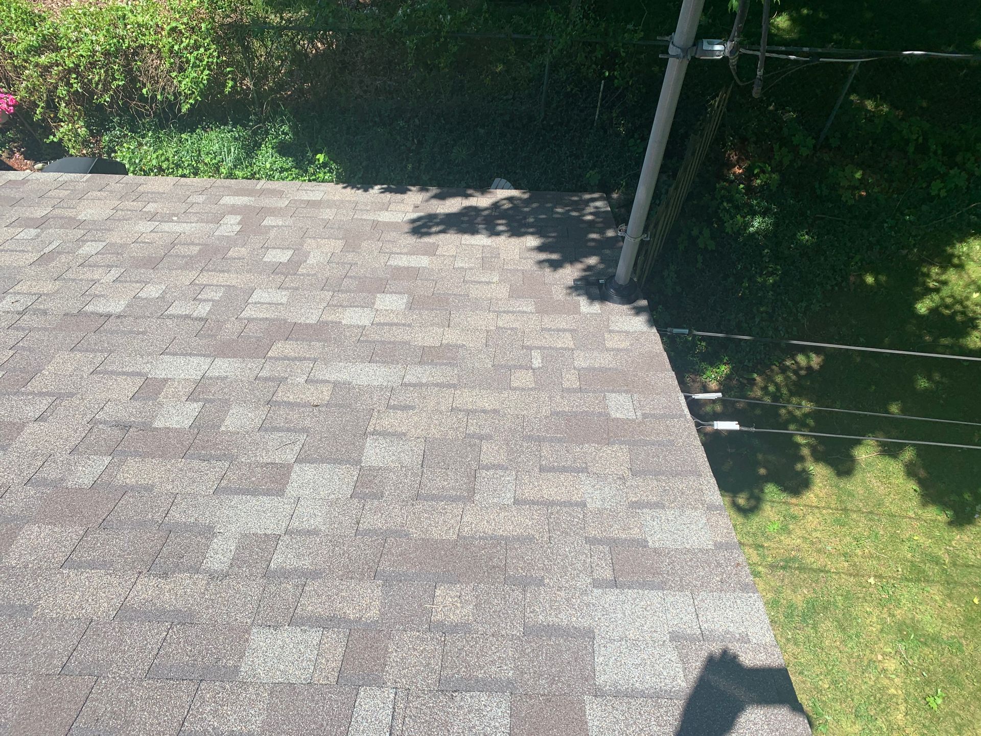 Gray shingled rooftop beside green lawn and trees, with a metal pole at the edge