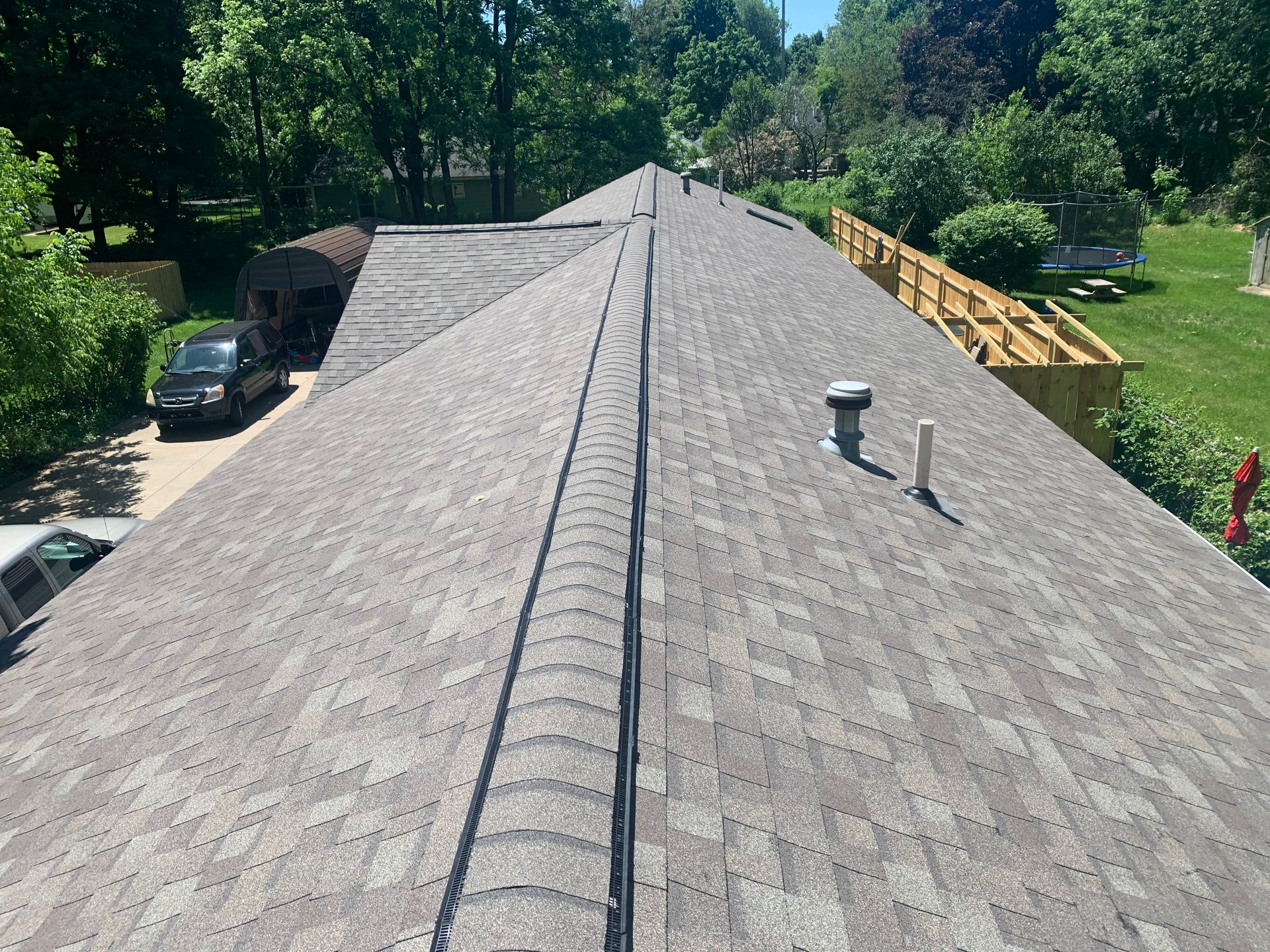 Roofing shingles on a house seen from above, with a vent and trees in the background.