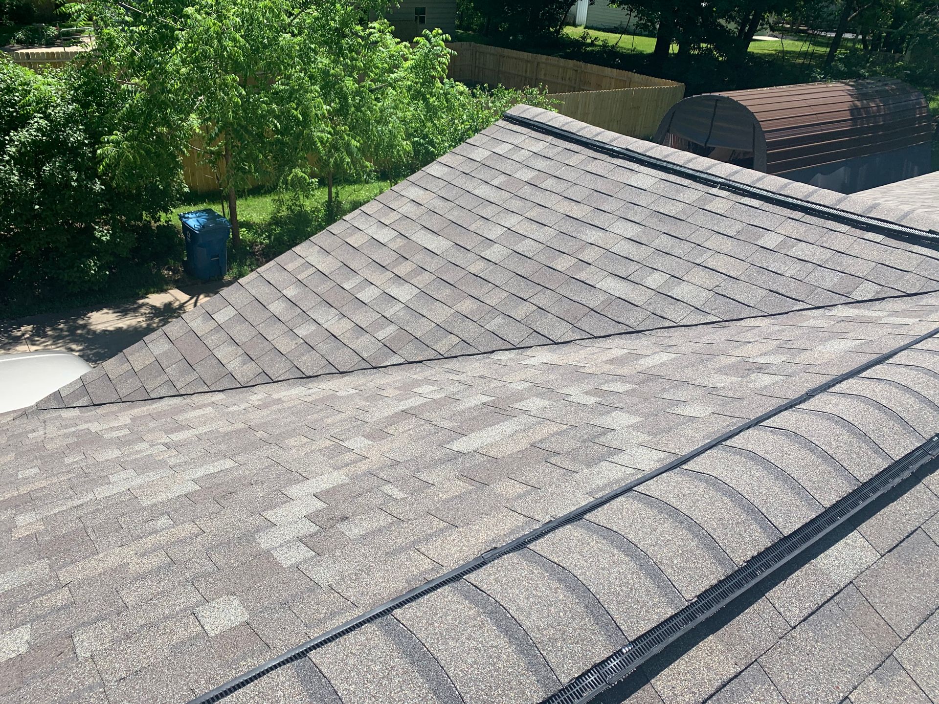 Gray shingled rooftops with a blue bin and leafy trees in the background