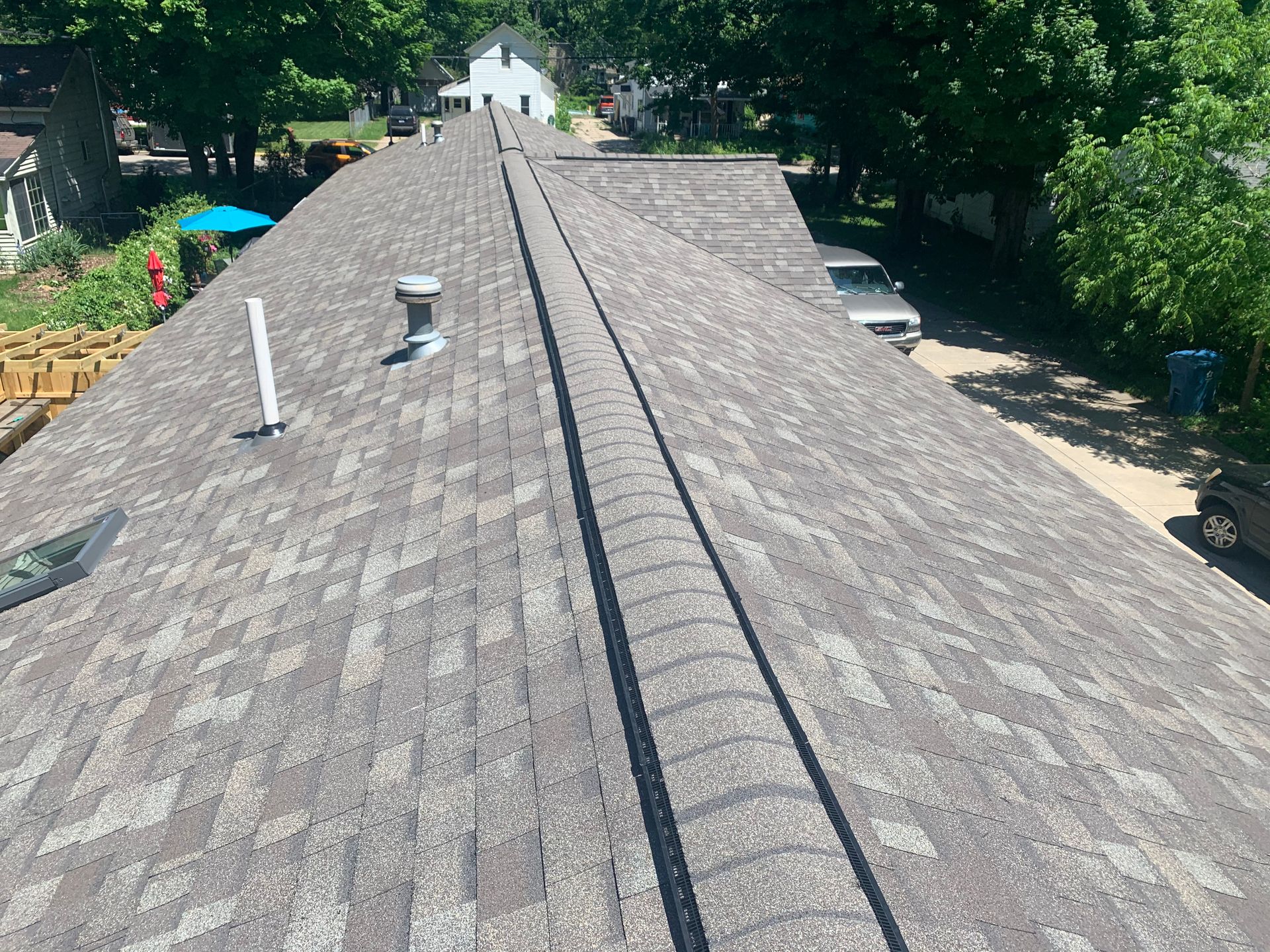 Roof shingles with a central ridge vent, viewed from above on a sunny day.