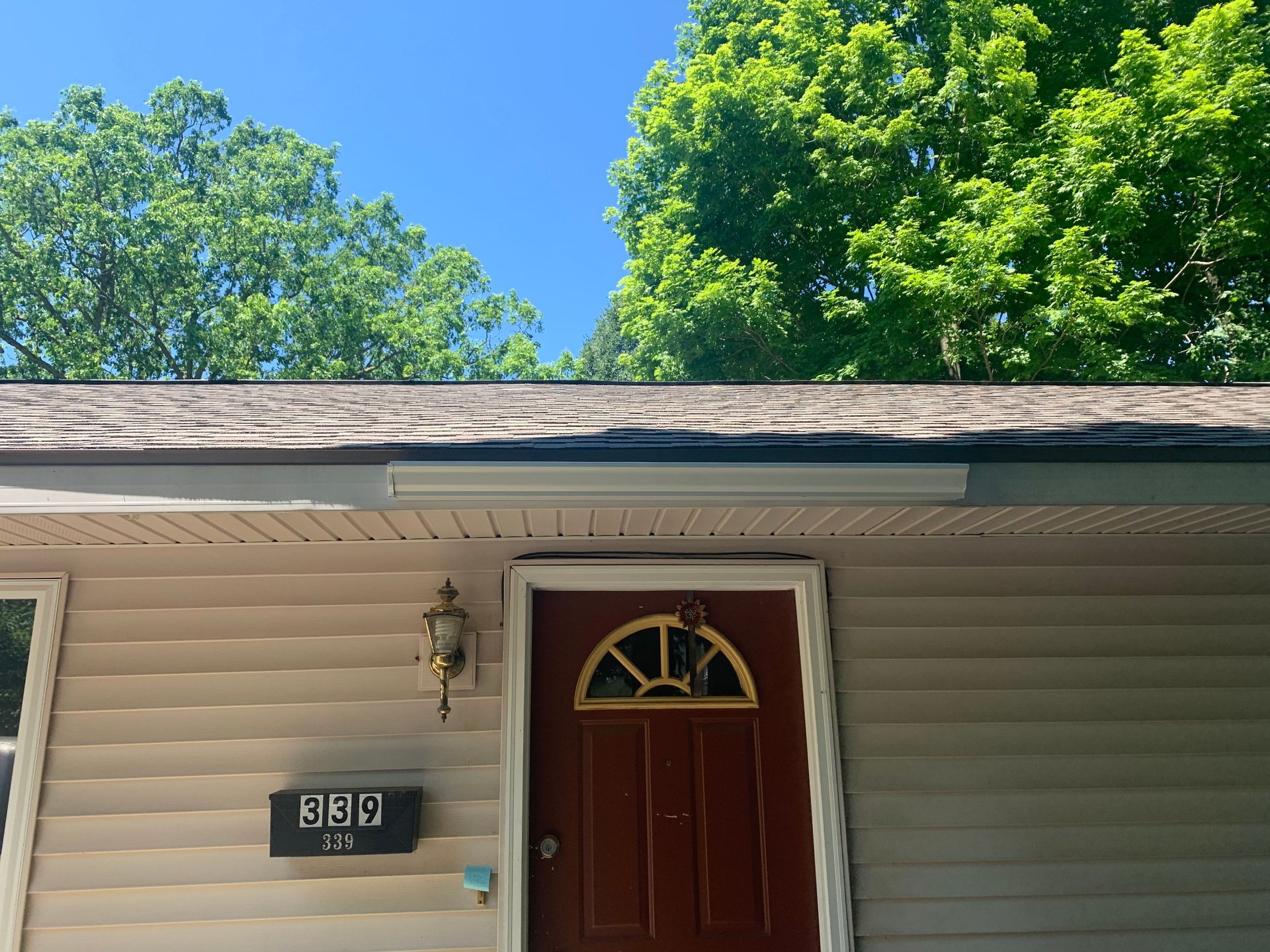House exterior with red front door, house number plaque, and green trees against a blue sky