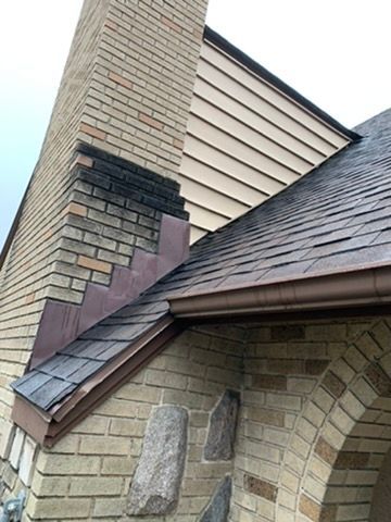 Damaged brick chimney with missing bricks and a dark patch above a shingled roof