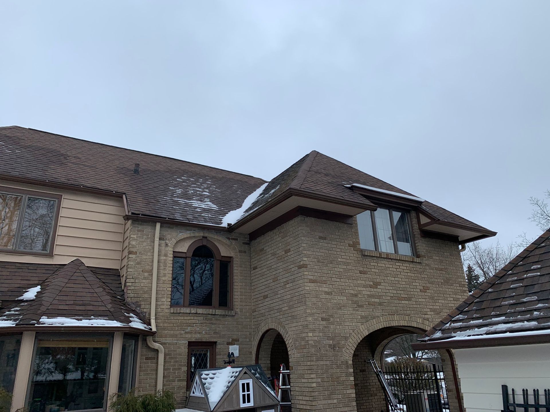 Stone house exterior with arched entry, brown tiled roof, and light snow on the ground
