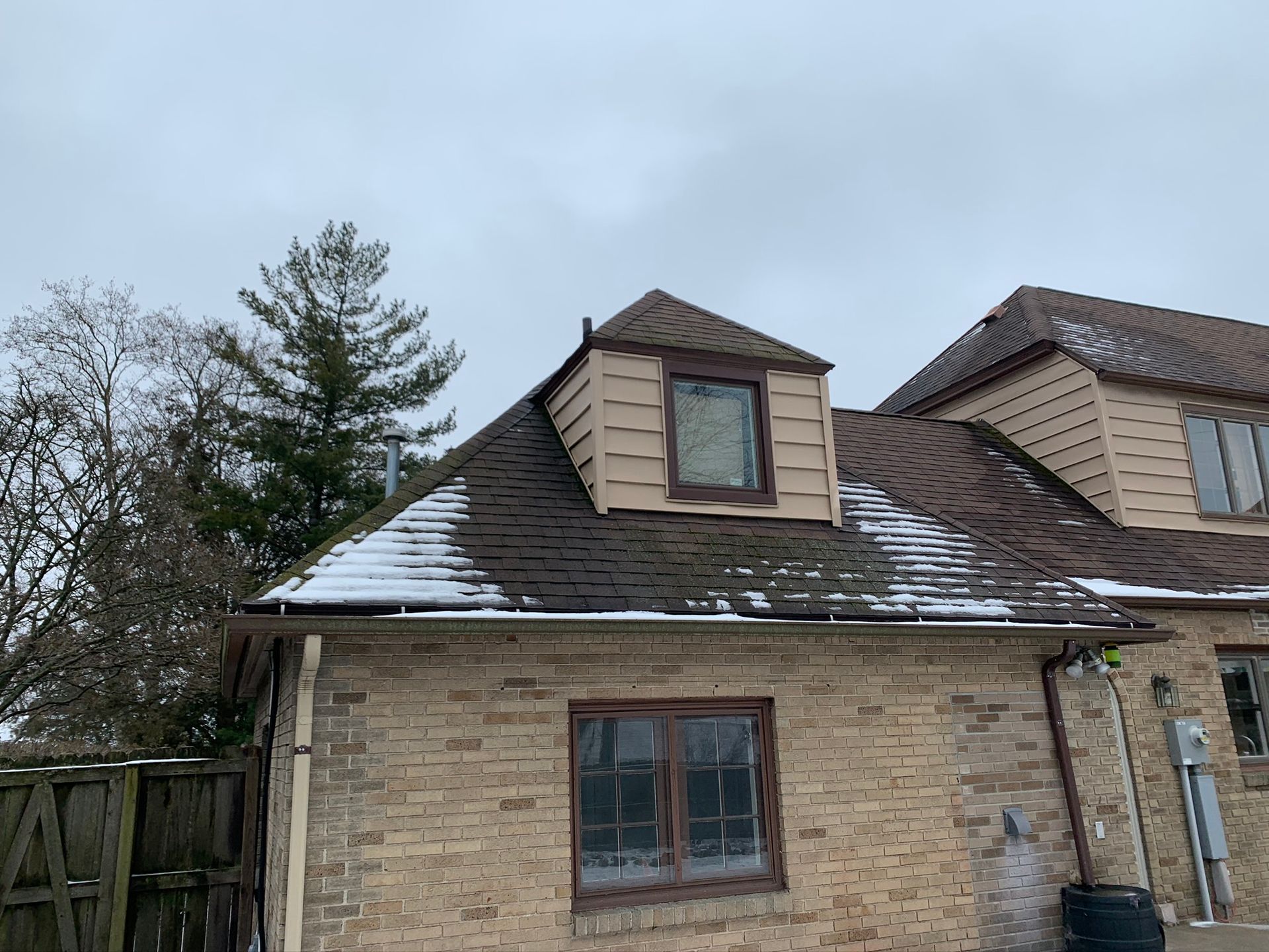 Brick house with snow on the roof and dormer windows under a cloudy sky