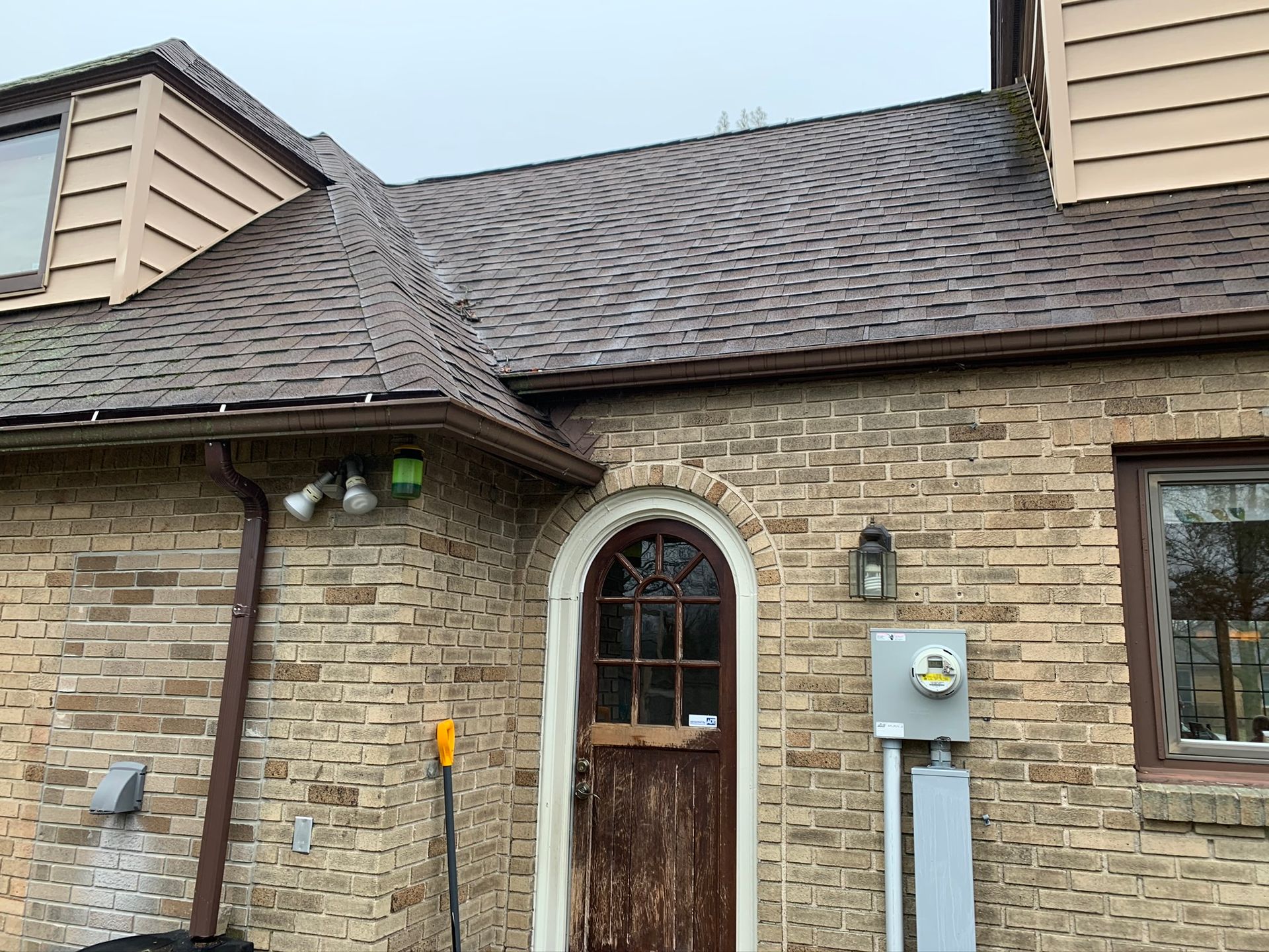 Brick house exterior with arched front door, roof shingles, and utility meter beside the entrance