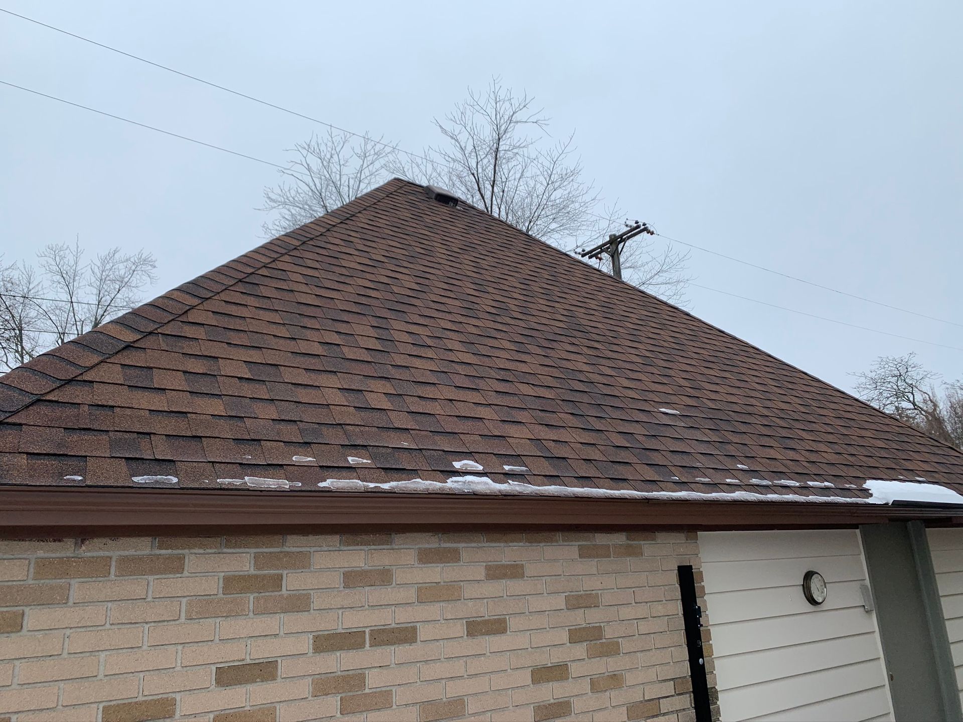 Brown shingle roof on a house with light brick walls and a small white side door under a cloudy sky