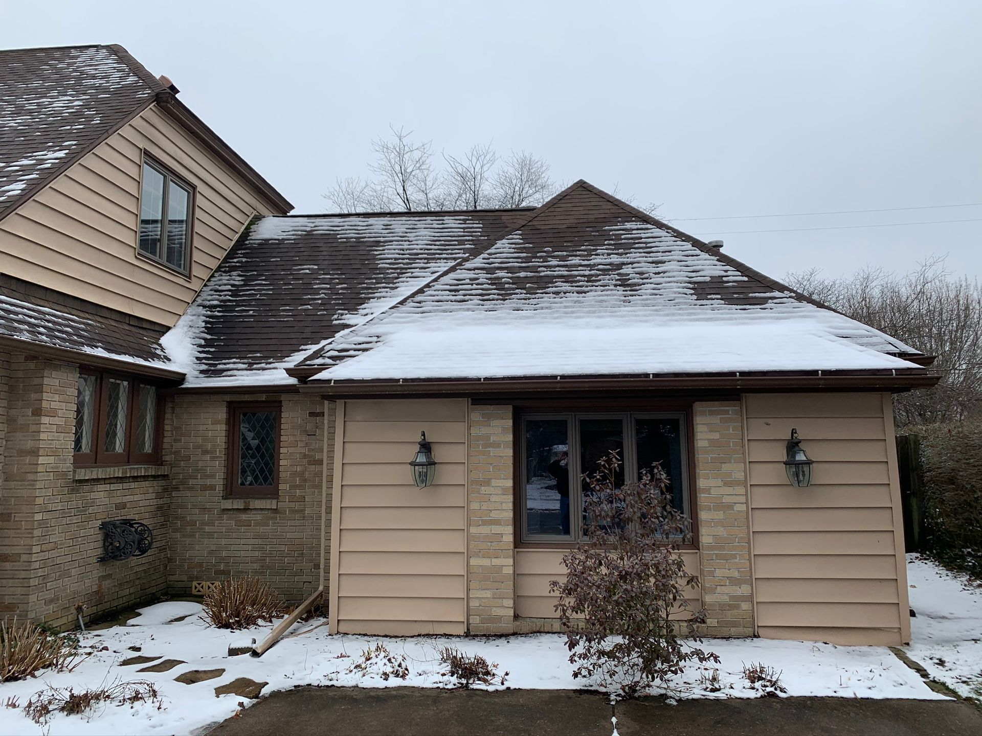 Snow-covered beige house with a dark roof and front window, viewed from the side in winter