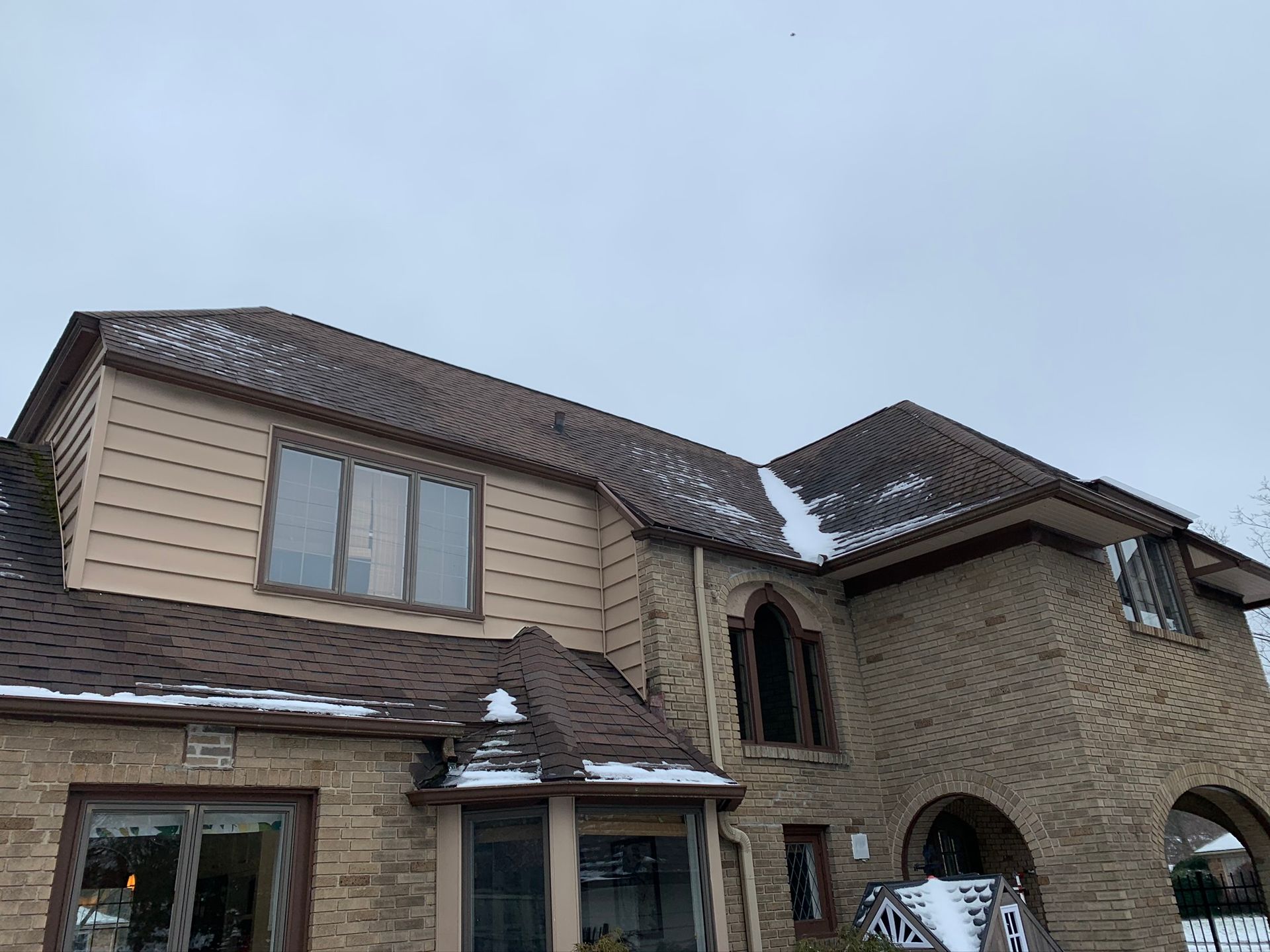 Large tan stone house with a tiled roof and arched entryway under a cloudy sky
