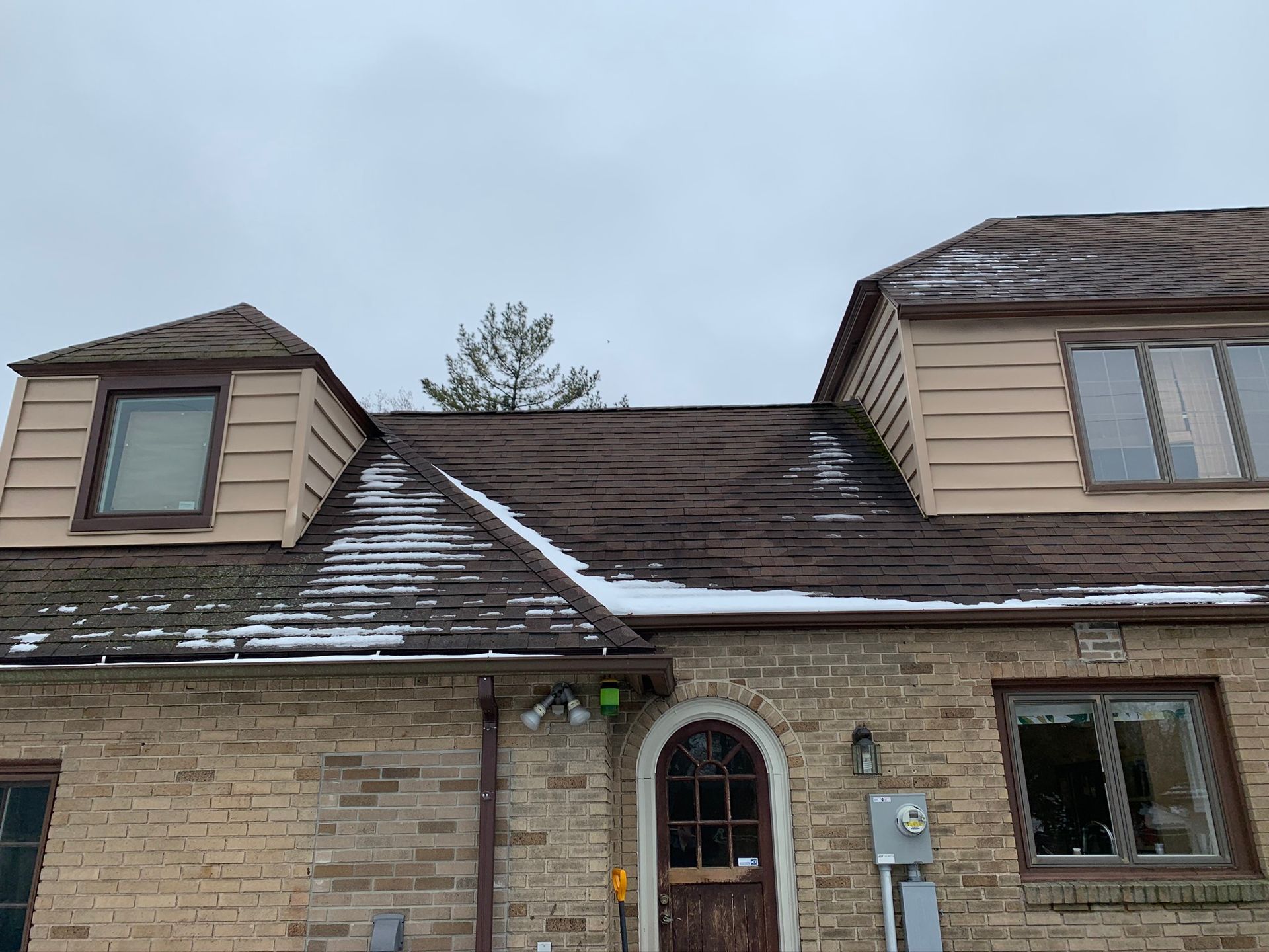 Brick house with a damaged shingled roof and light snow on the eaves