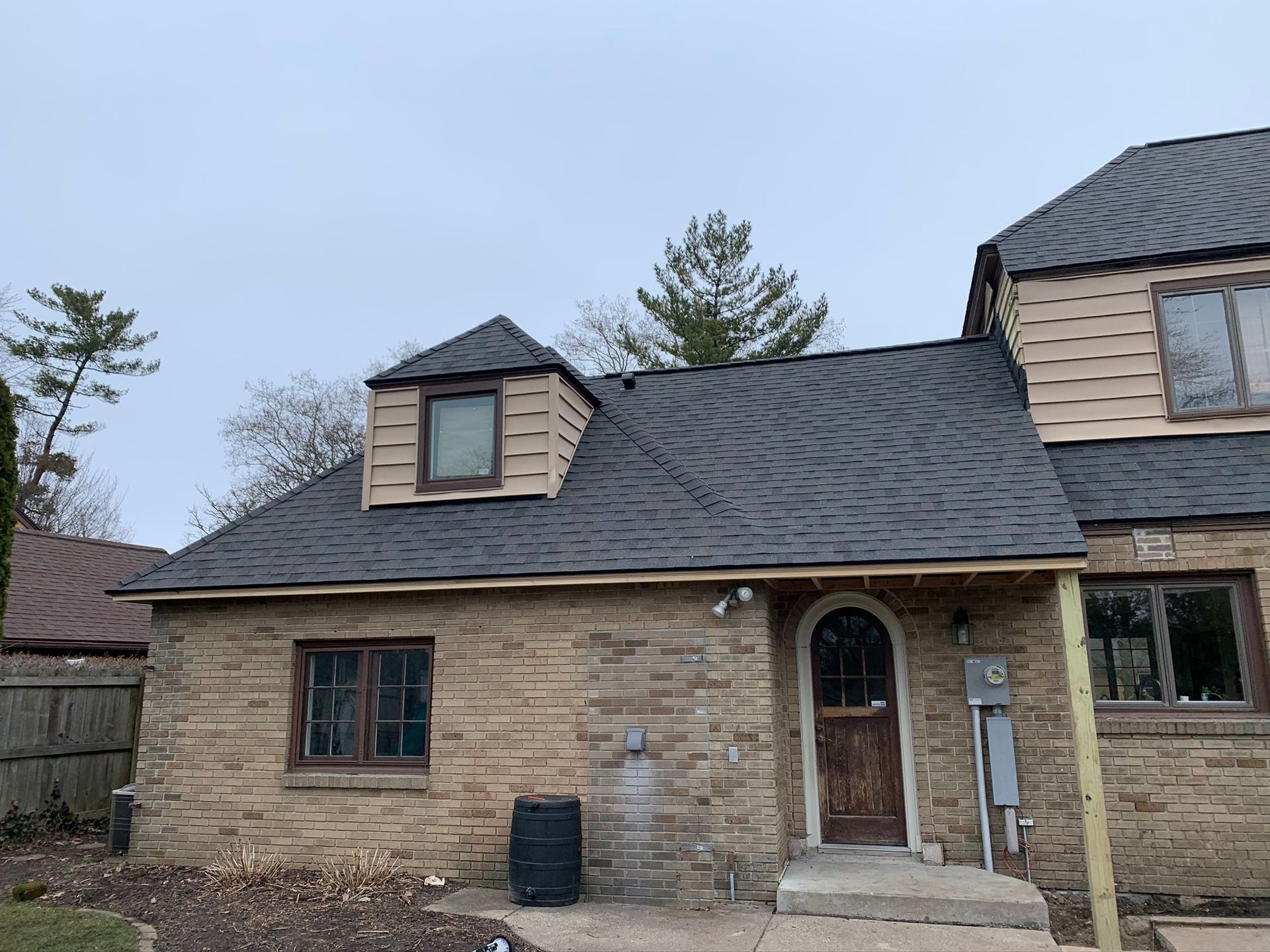 Stone house exterior with dark shingle roof and small dormer windows on a cloudy day