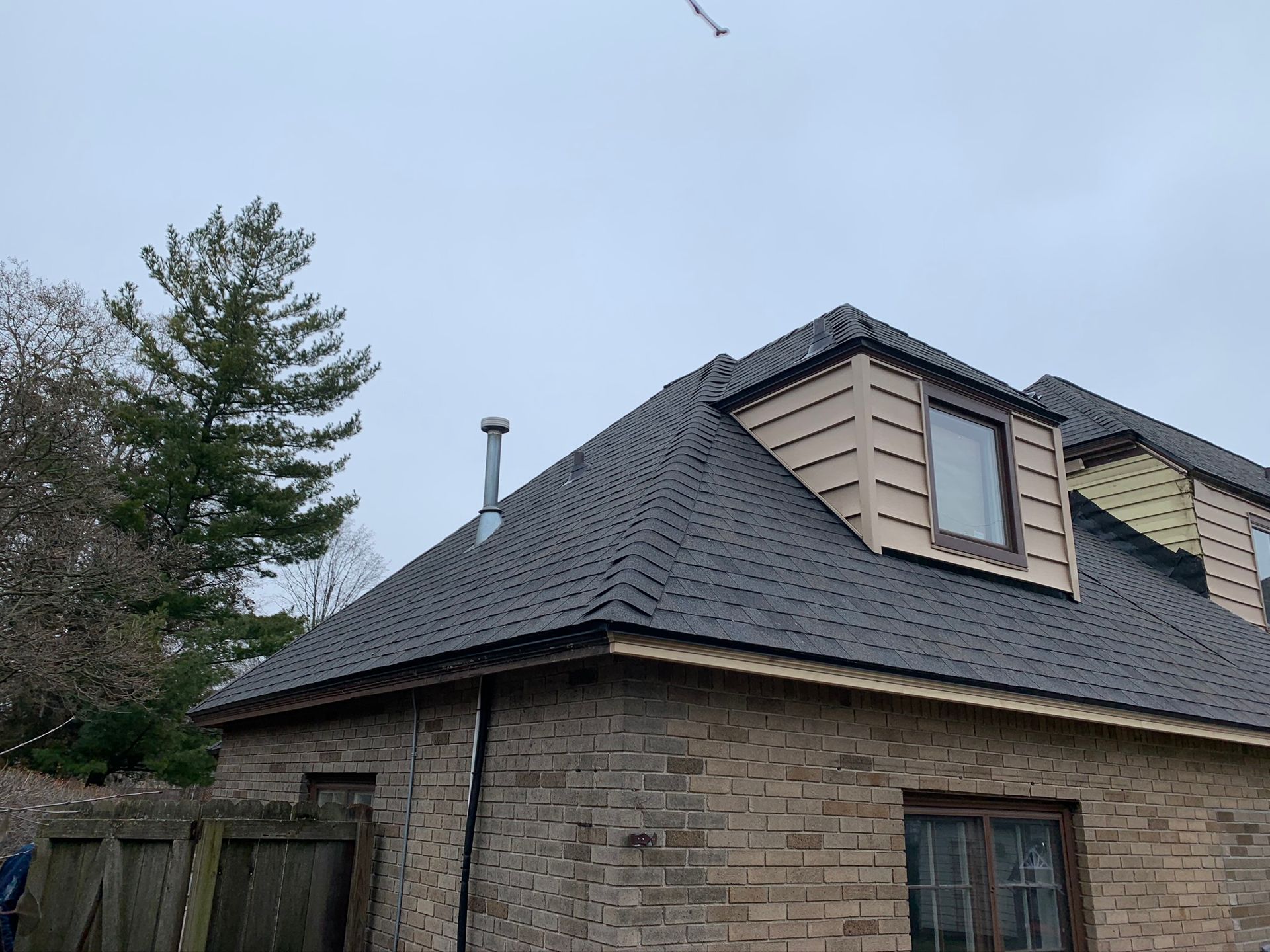 Brick house with dark shingled roof and dormer windows under a cloudy sky