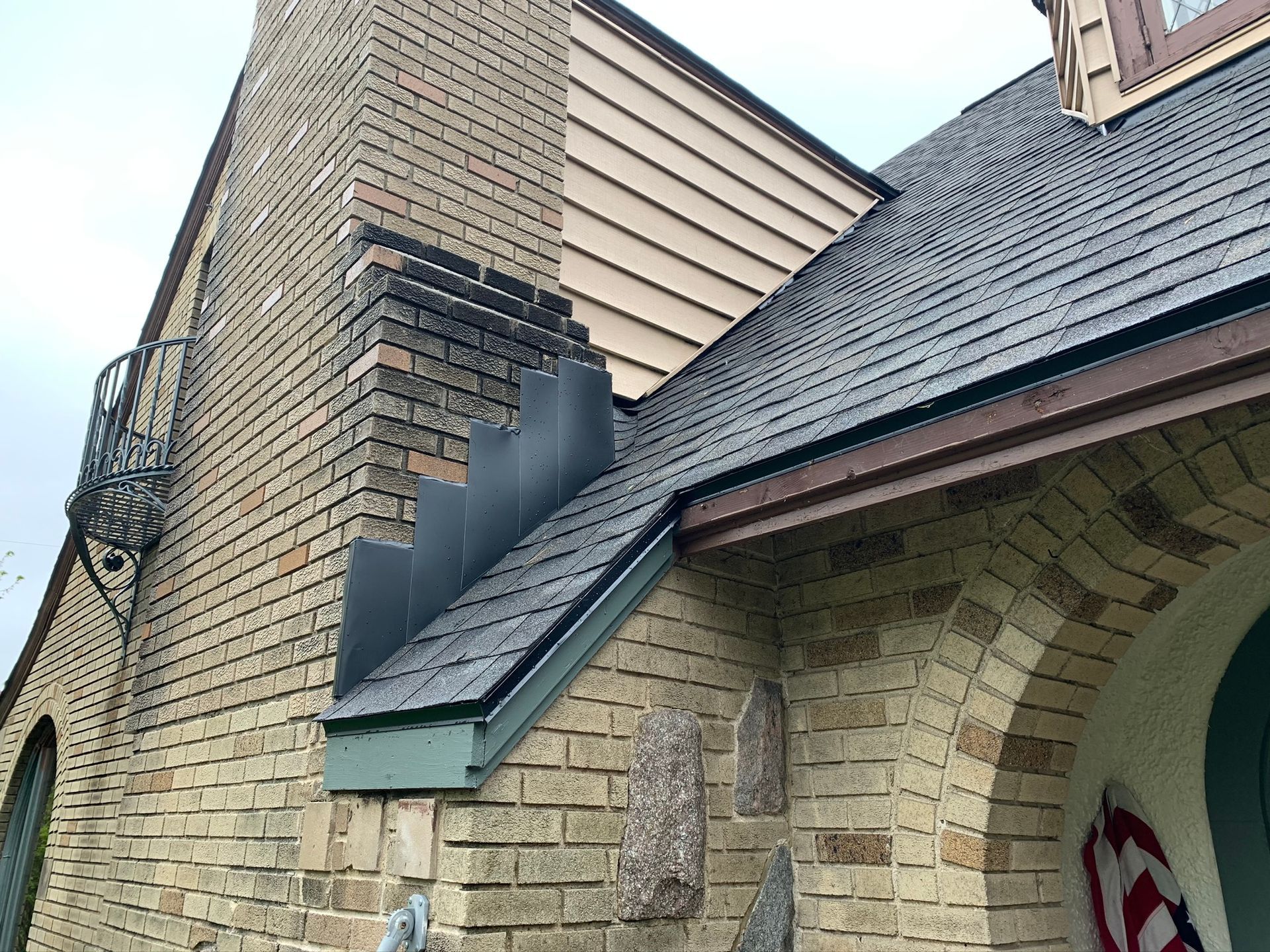 Brick house roof with dark shingles, chimney, and arched porch overhang