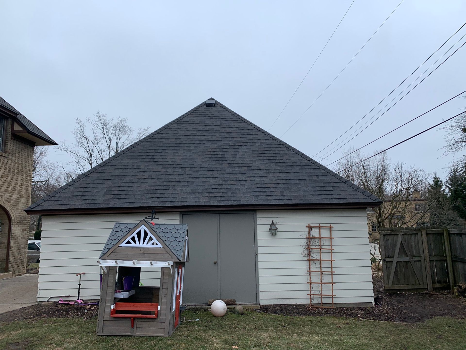 Backyard with white garage, small playhouse, and trellis against a cloudy sky