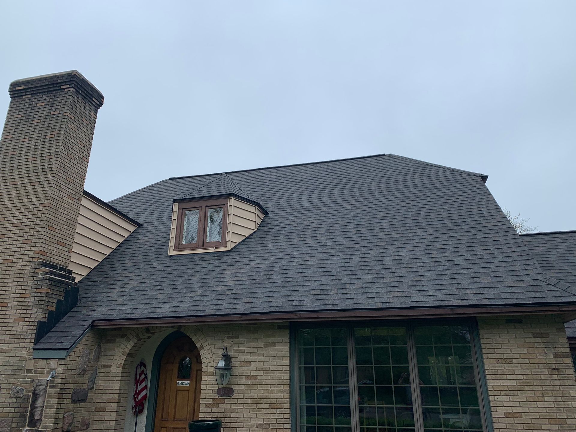 Stone house exterior with dark shingled roof and brick chimney under a cloudy sky