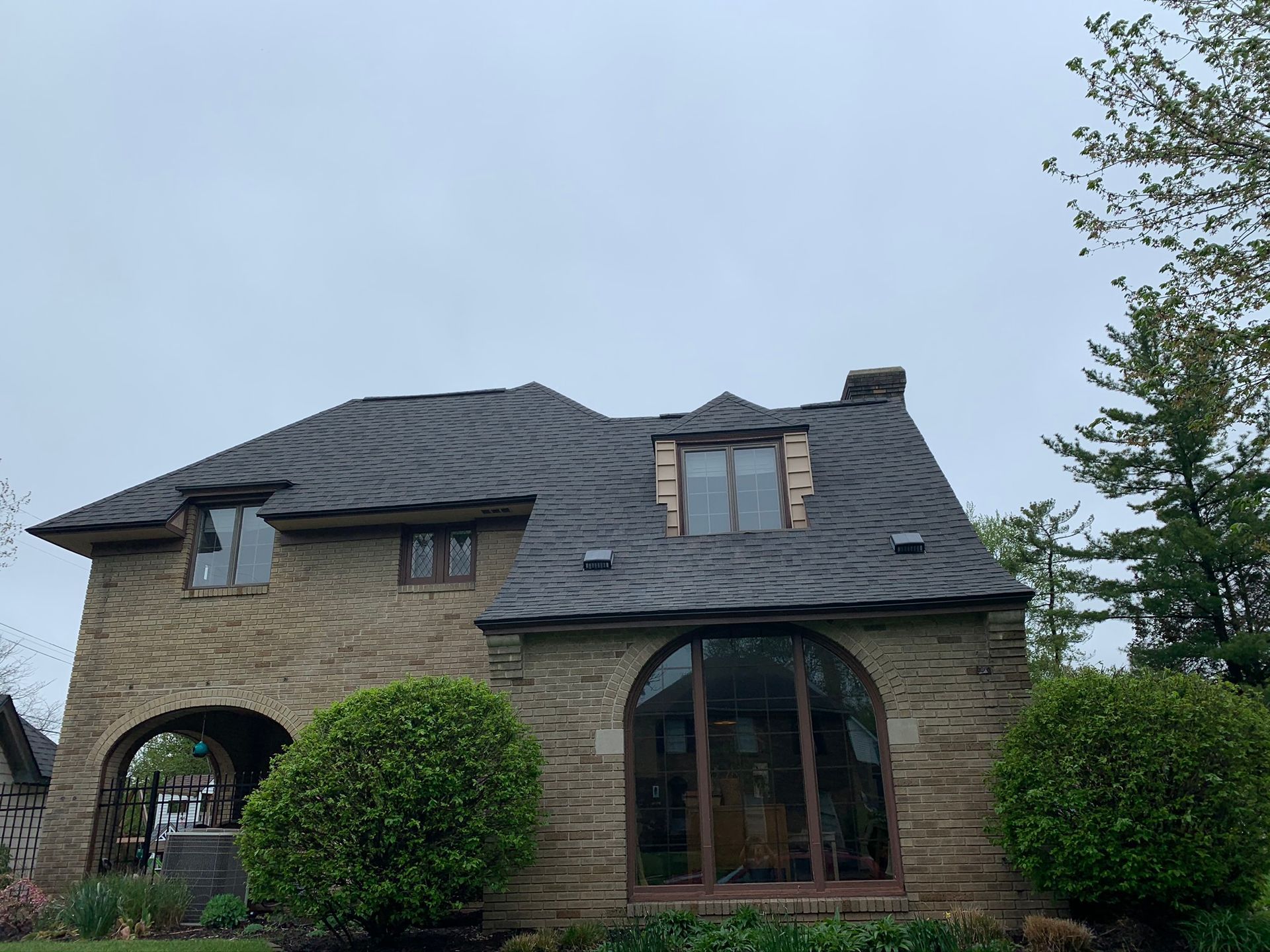 Stone house with dark roof, arched windows, and trimmed bushes under a cloudy sky