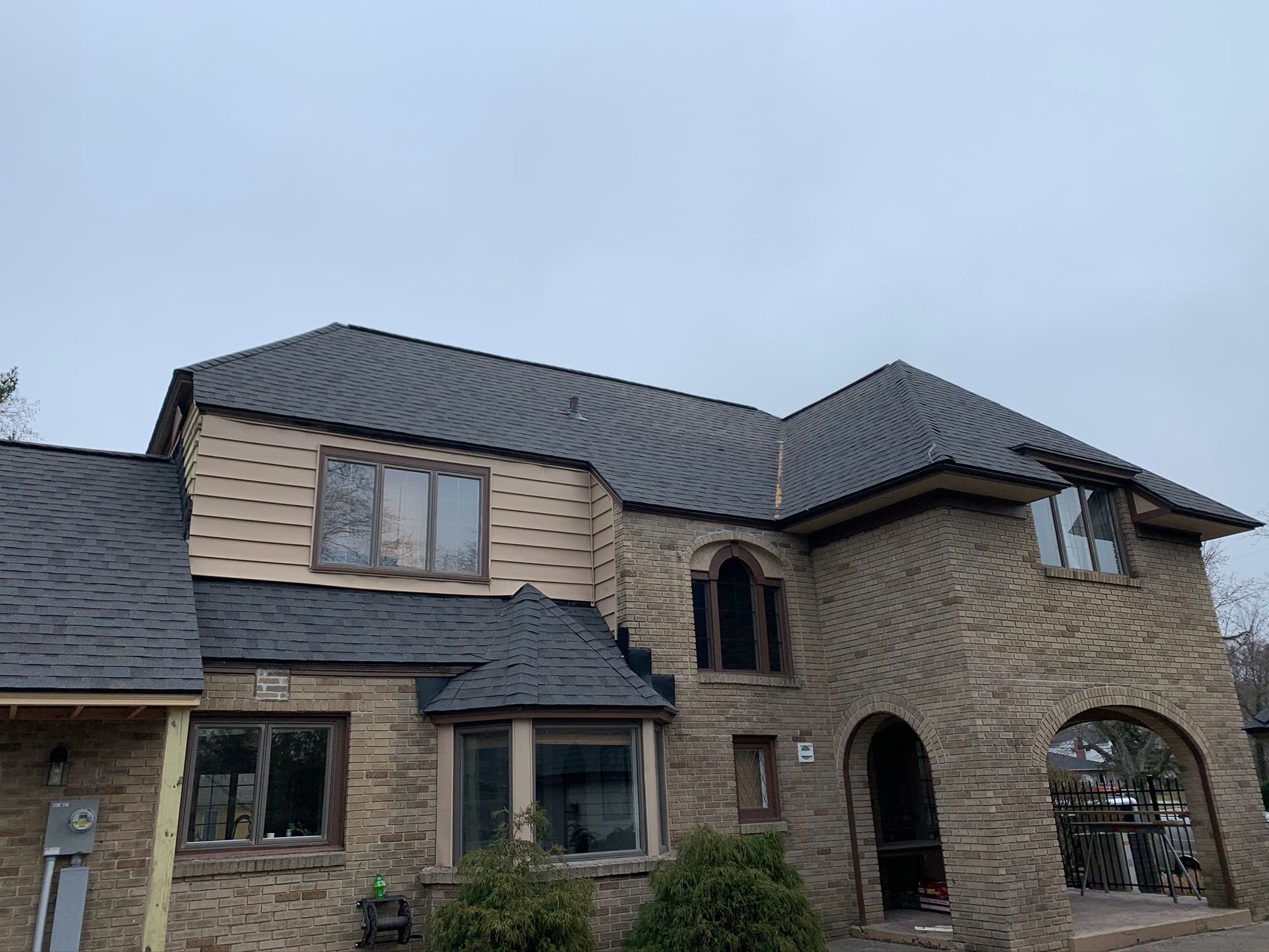Large stone house with dark roof and arched entryway under a cloudy sky