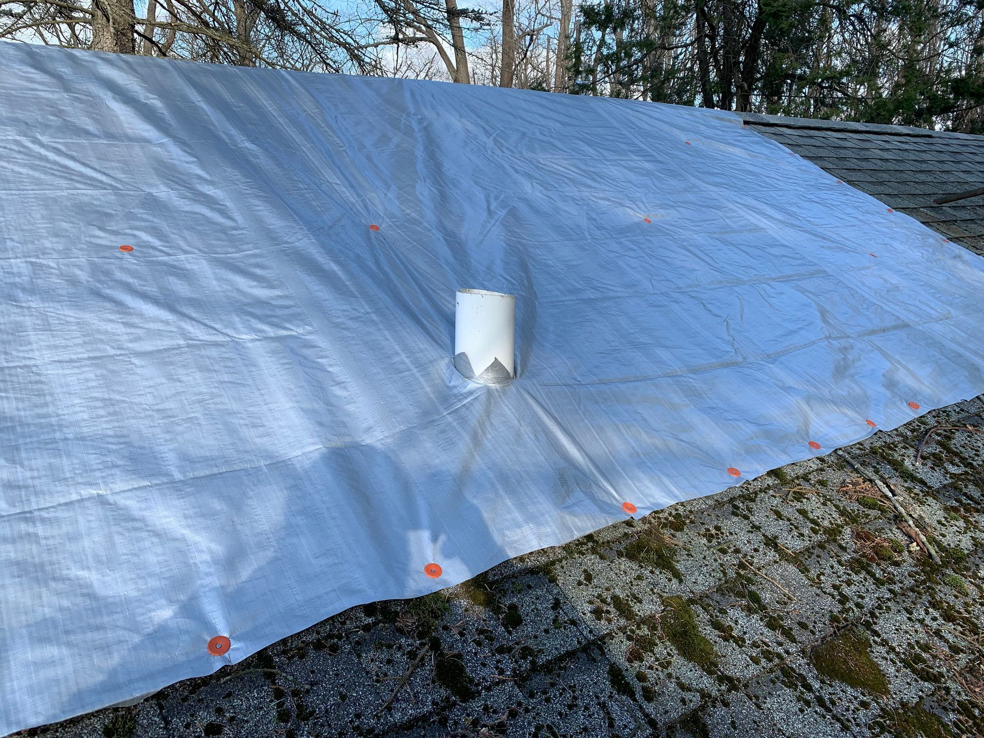 Blue tarp stretched over a sloped roof with a white vent pipe near the center.