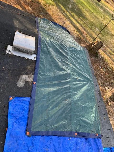 Blue tarp and green tarp laid out on grass and pavement beside a wooden post.