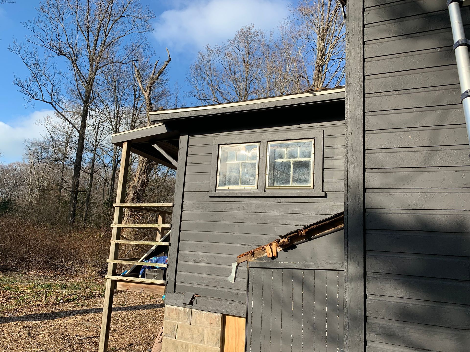 Gray house exterior with ladder leaning beside a window under a blue sky