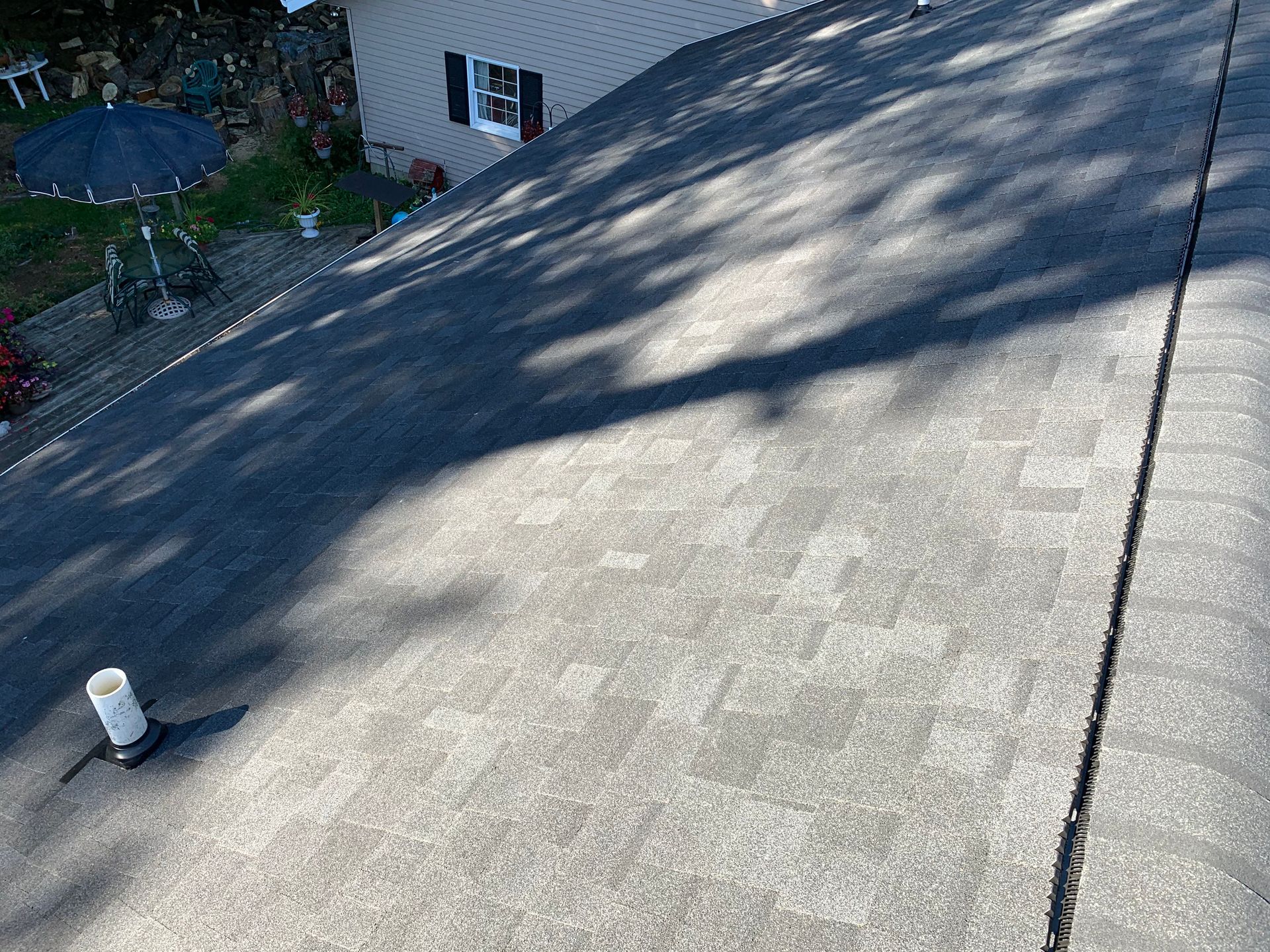Sunlit sloped concrete roof with tree shadows and a small white vent pipe near the edge