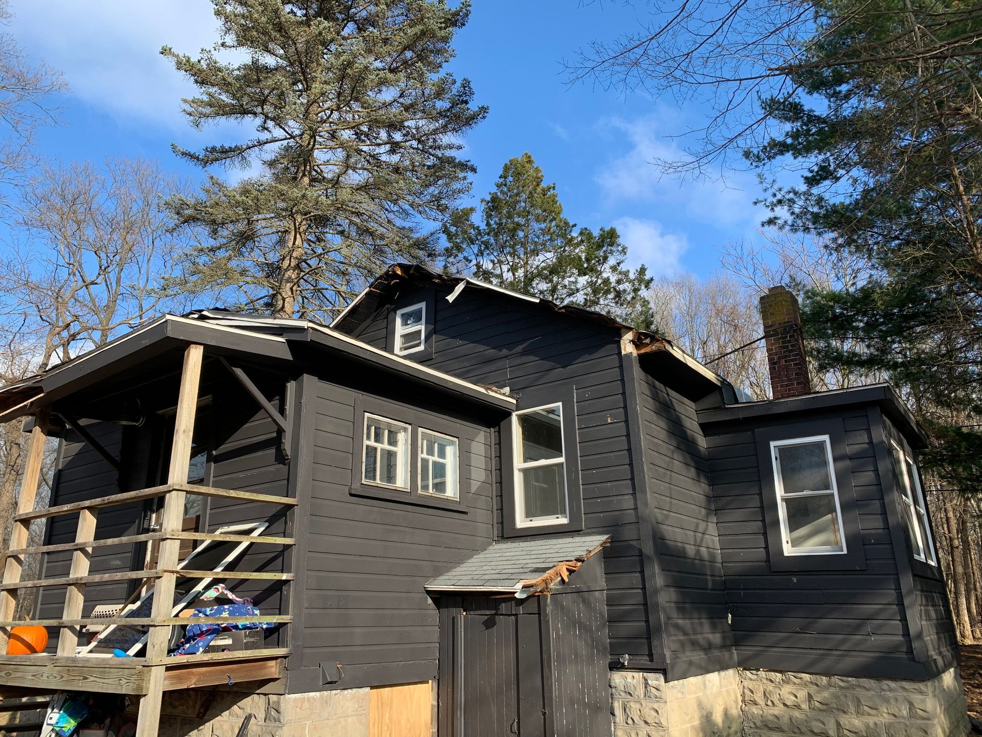 Dark gray house exterior with porch and tall trees under a blue sky