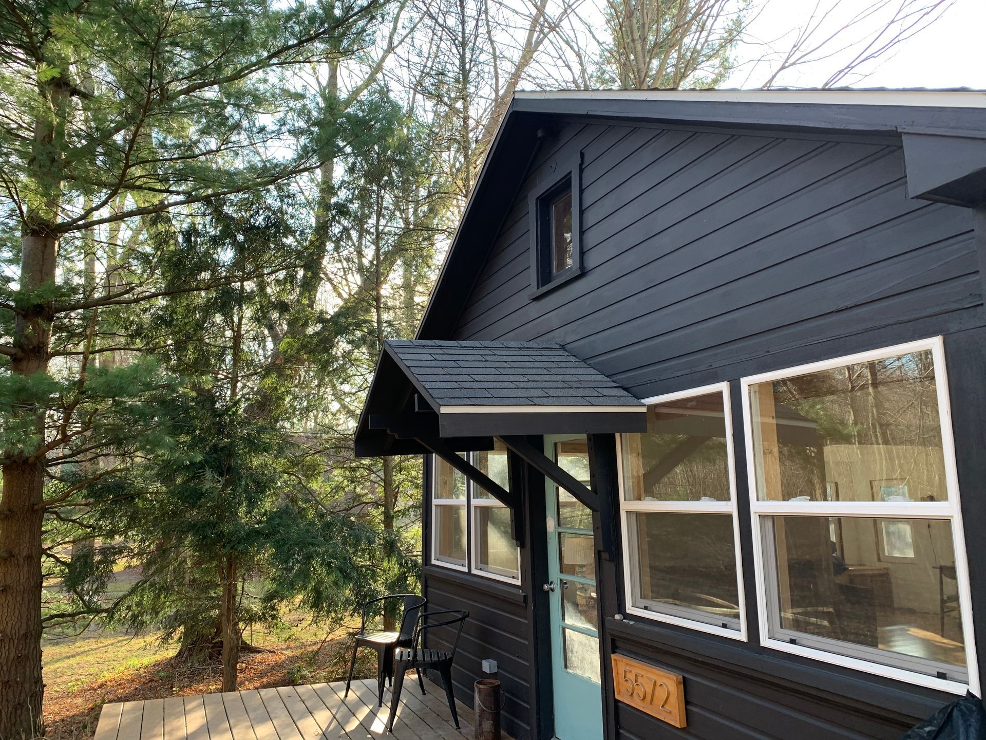 Dark blue house exterior with a small porch, windows, and trees beside it