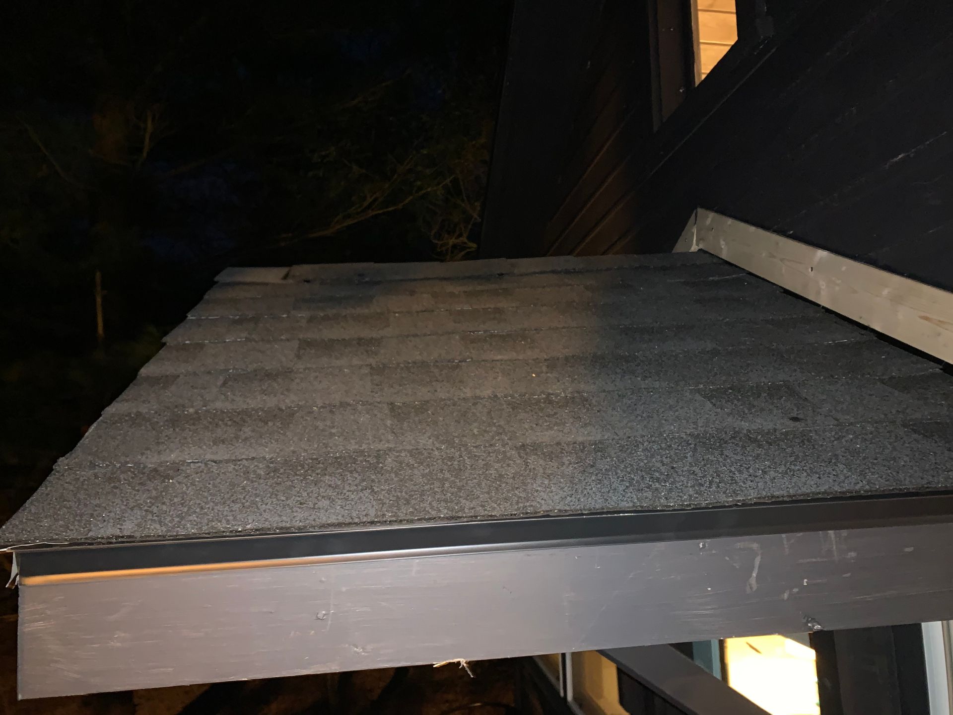 Gray roof shingles on a small flat rooftop at night, lit by a camera flash.