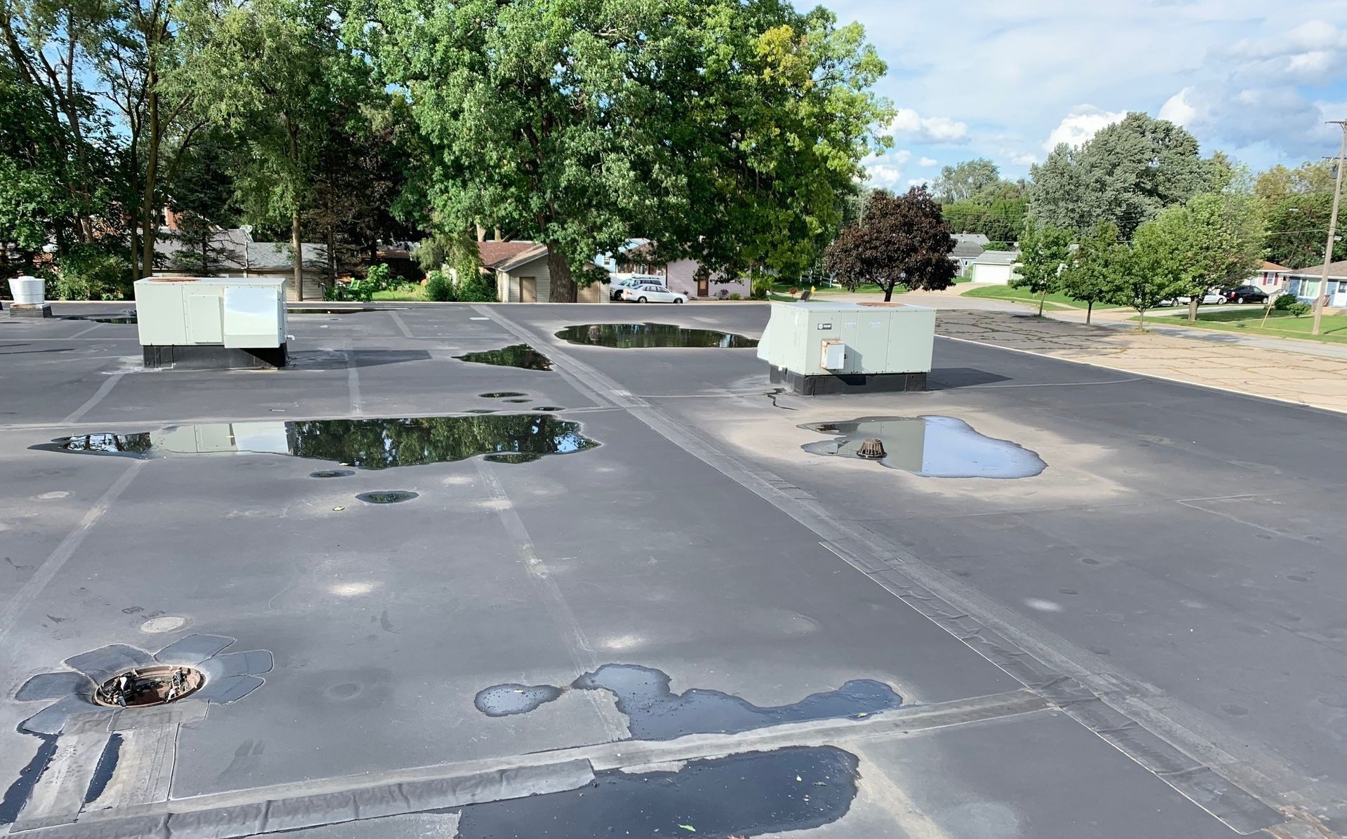 Flat rooftop with puddles and HVAC units under a clear sky.