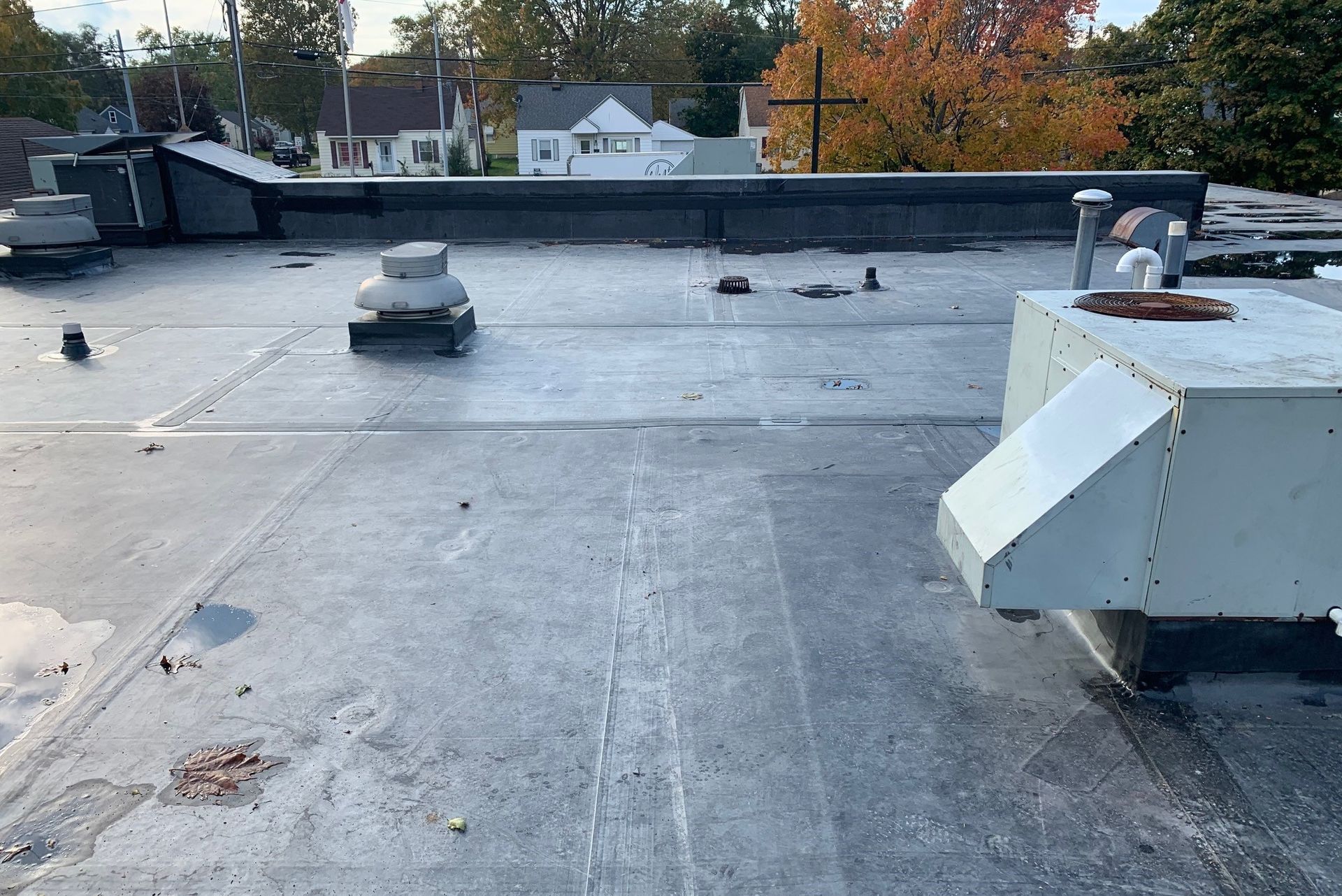 Flat rooftop with vents and HVAC units, viewed under overcast light with trees and houses in the background