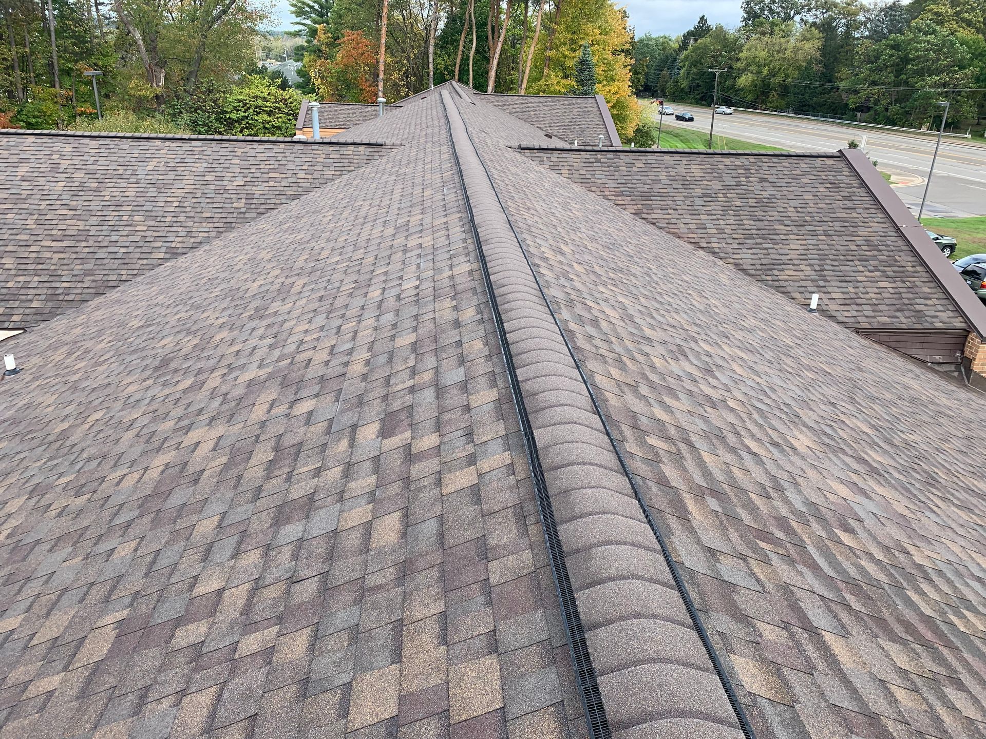 Gray shingled roof with a central ridge, viewed from above against a tree-lined background