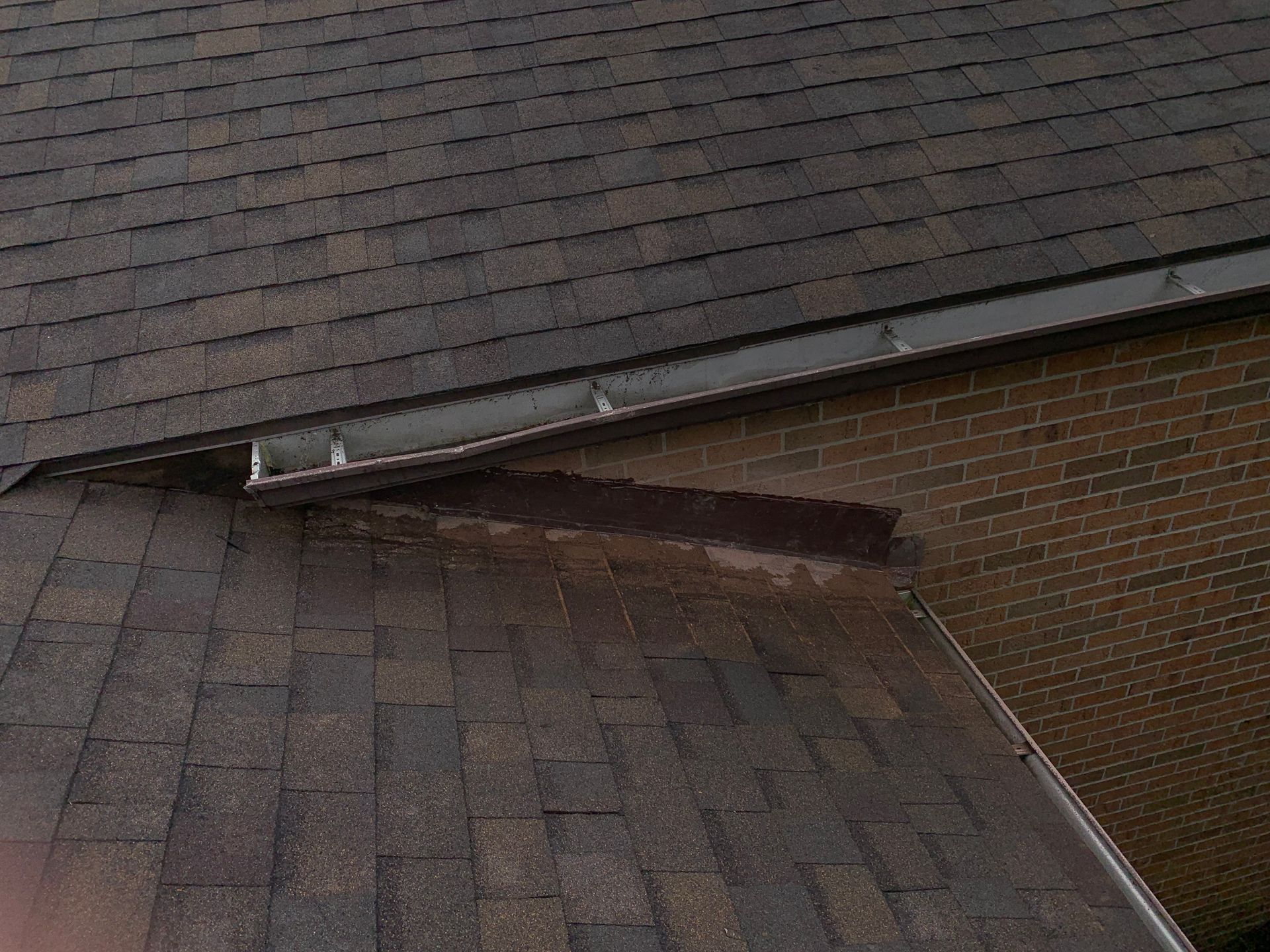 Damaged roof shingles with a large gap and exposed underlayment near the edge