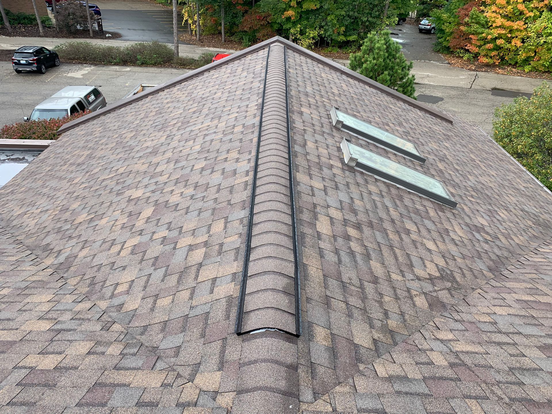 Aerial view of a shingled roof with two skylights and a central ridge vent.