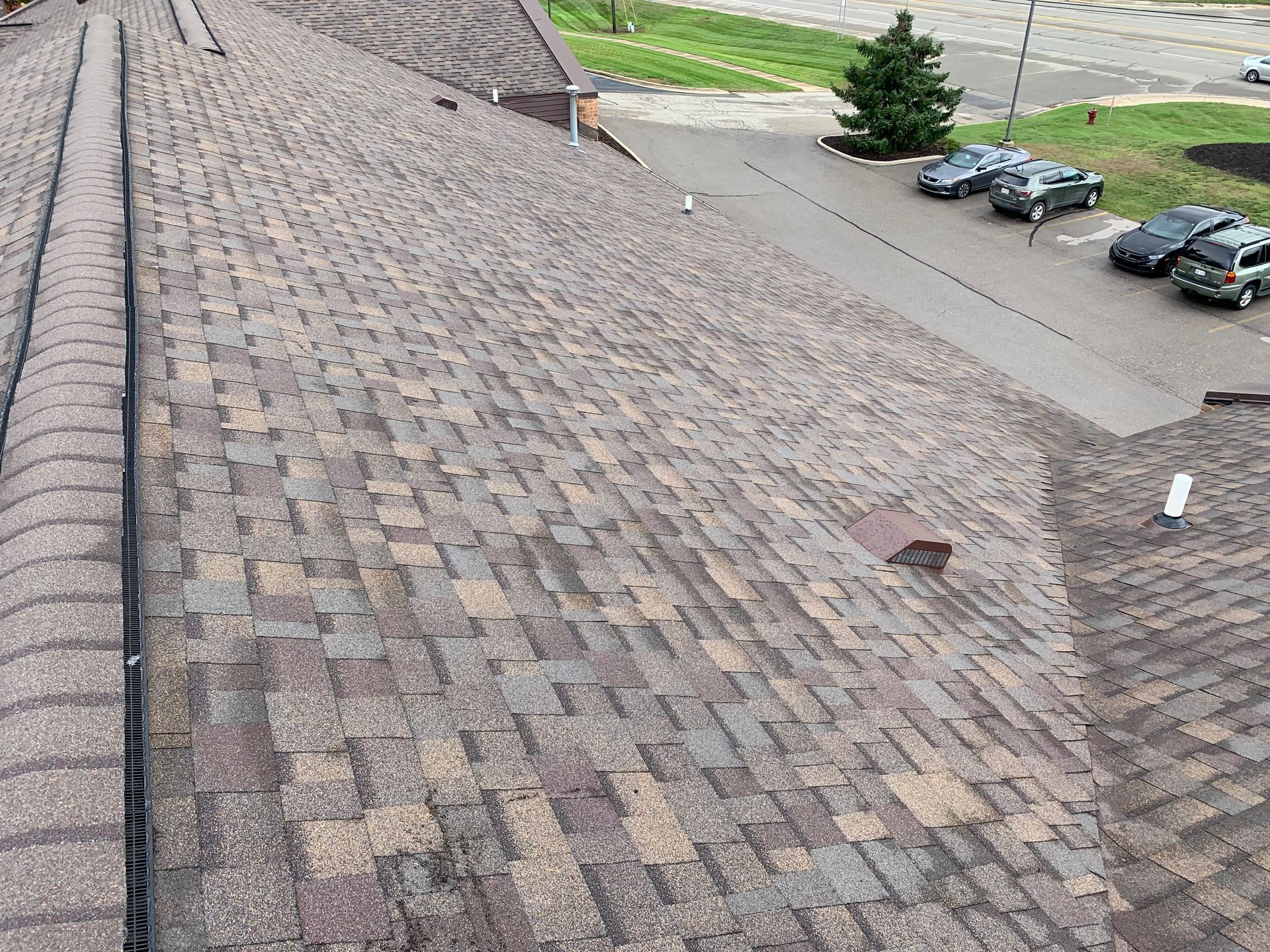 Rooftop with weathered shingles beside a parking lot with several cars.