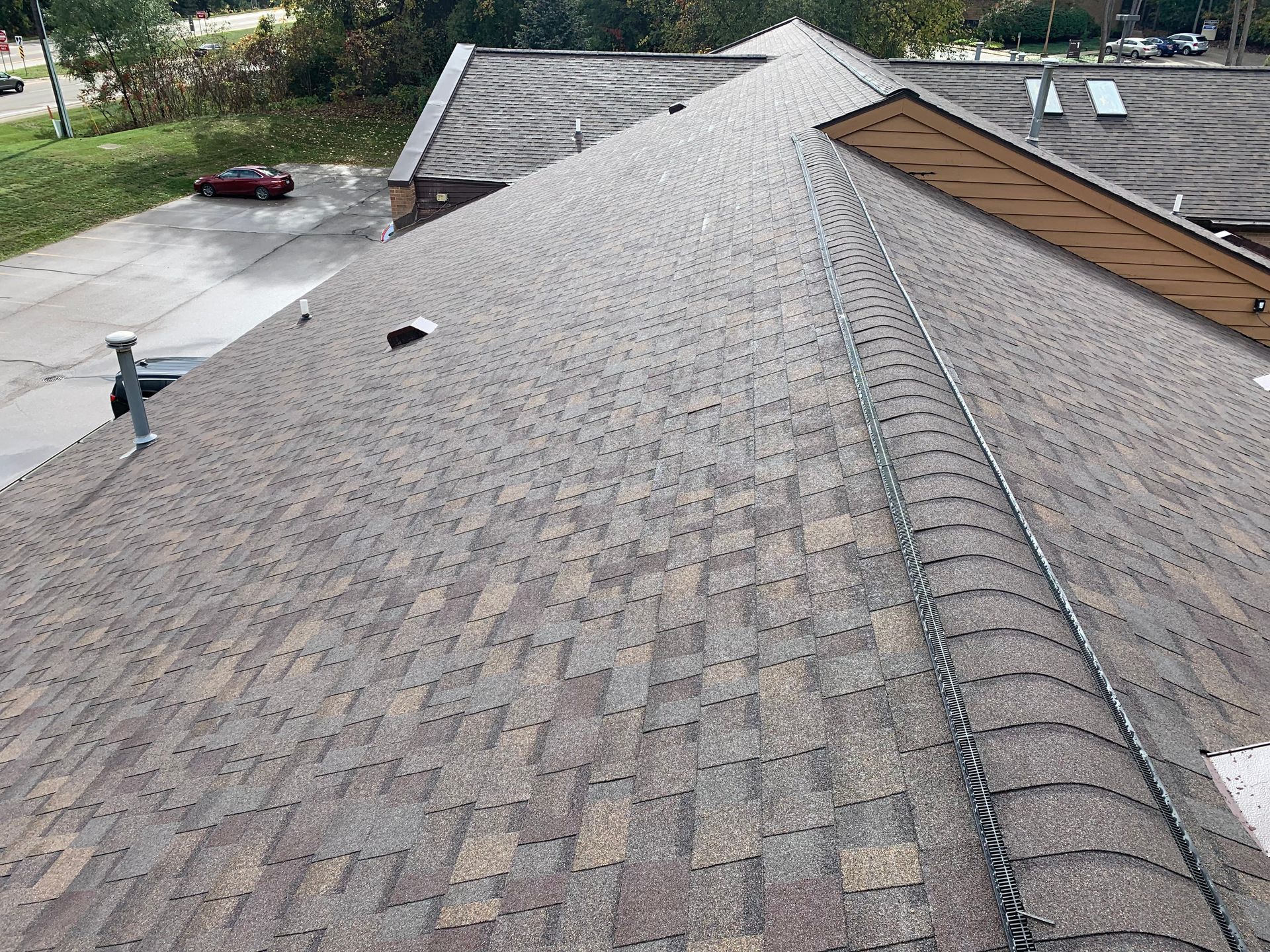 Roof shingles on a house with a roof vent and neighboring rooftops in view