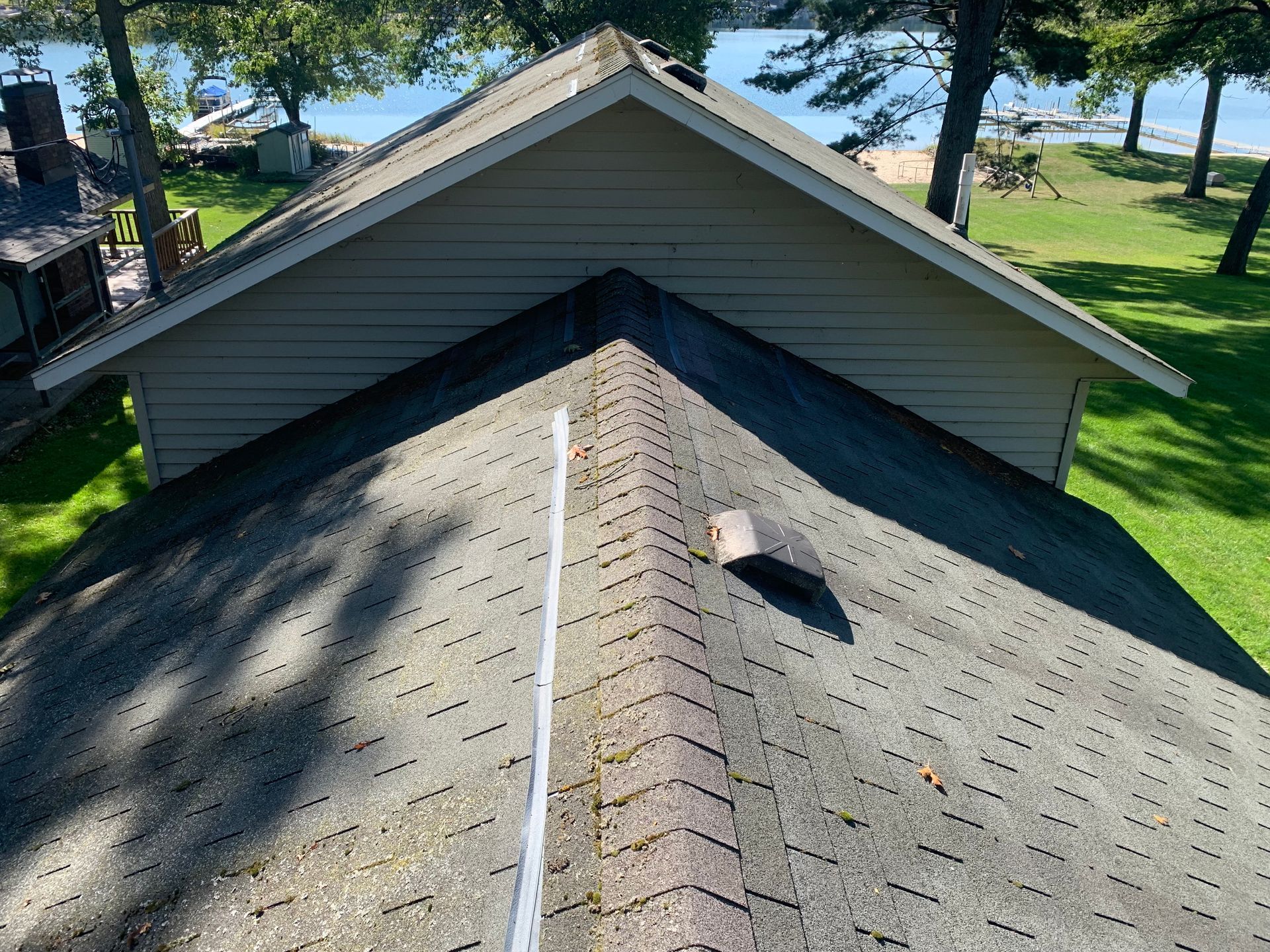 View from rooftop shingles toward a lakeside yard with trees and grass