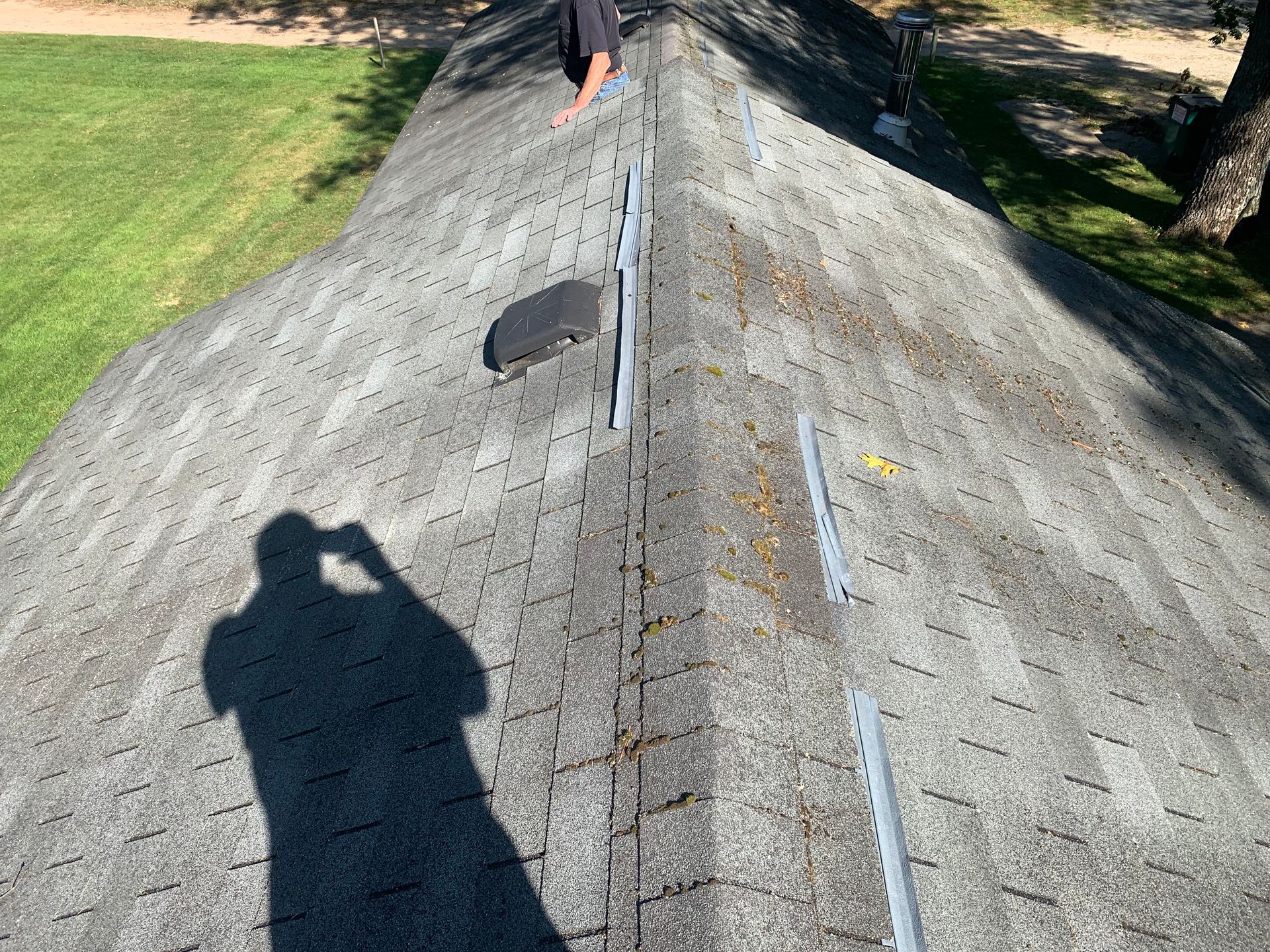 Roof inspection on a shingled roof with a person near the ridge and a shadow in the foreground