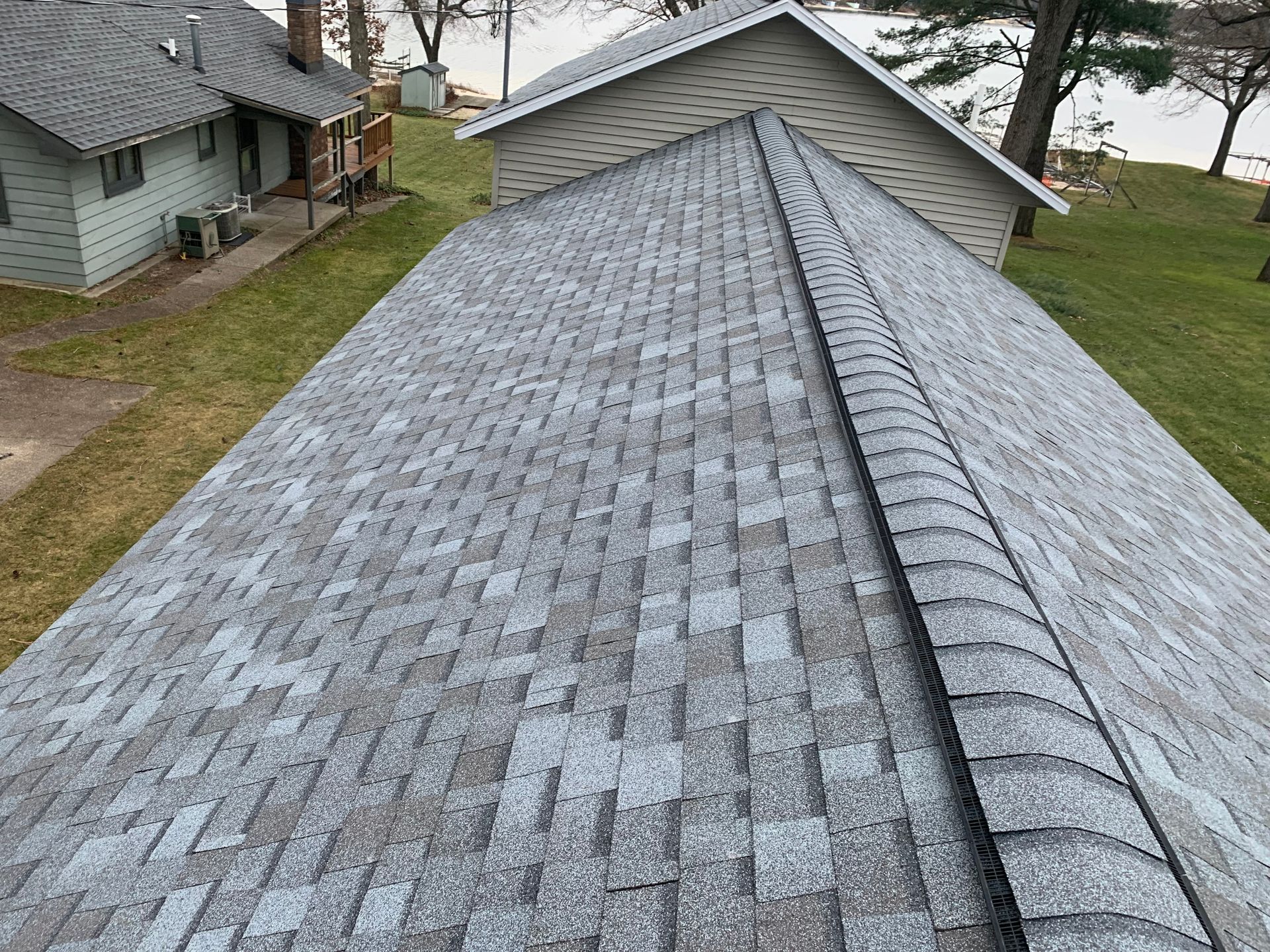 Roof covered in gray shingles on a house near water and neighboring homes