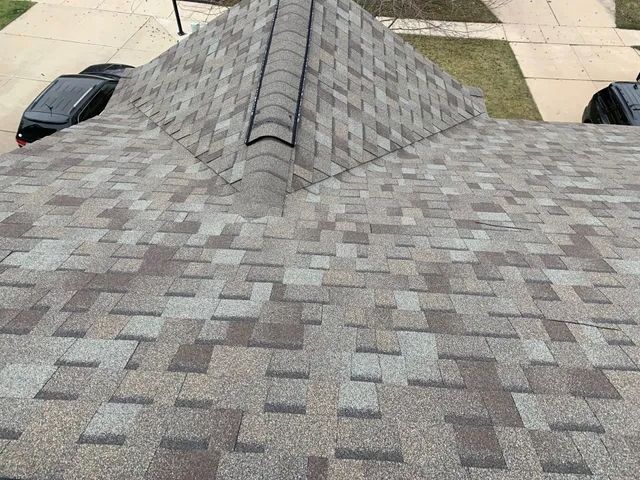Close-up of a textured gray stone wall with rooftops and a yard visible at the bottom edges