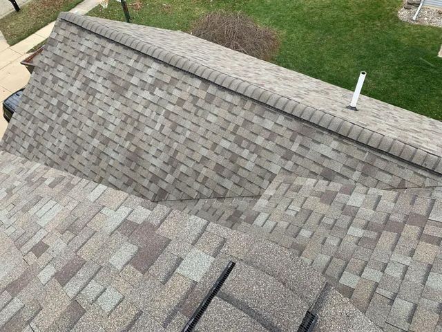 Close-up of a gray shingled roof beside a green lawn and brick walkway.