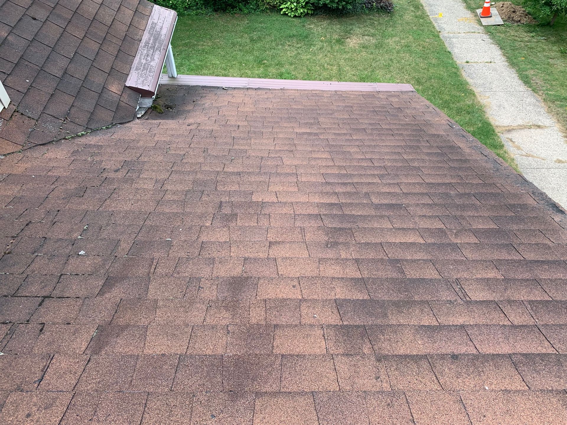 Weathered shingled roof with mossy patches beside a grassy yard and sidewalk