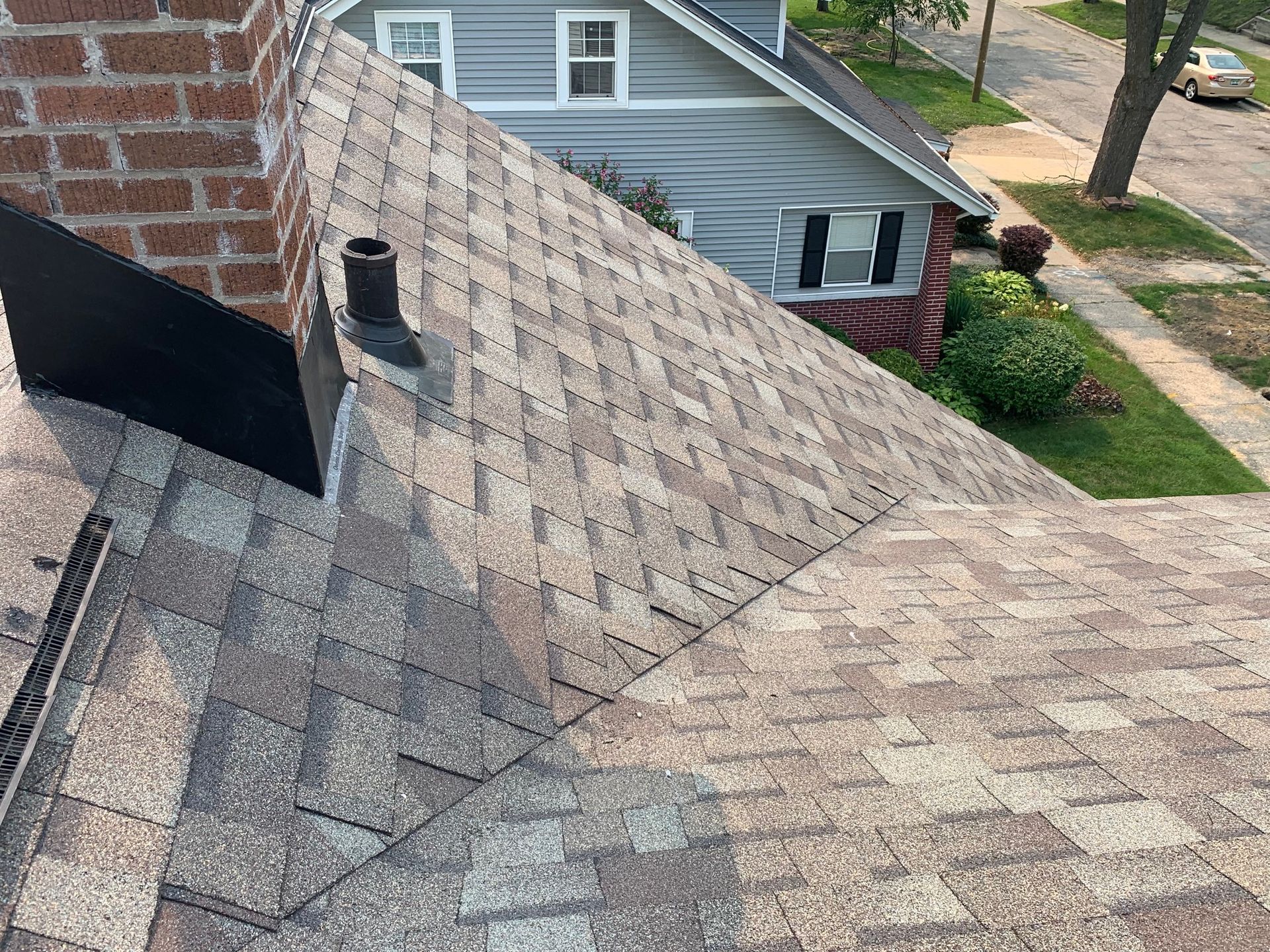 Roof shingles with visible weather damage and a black vent chimney on a suburban house roof.
