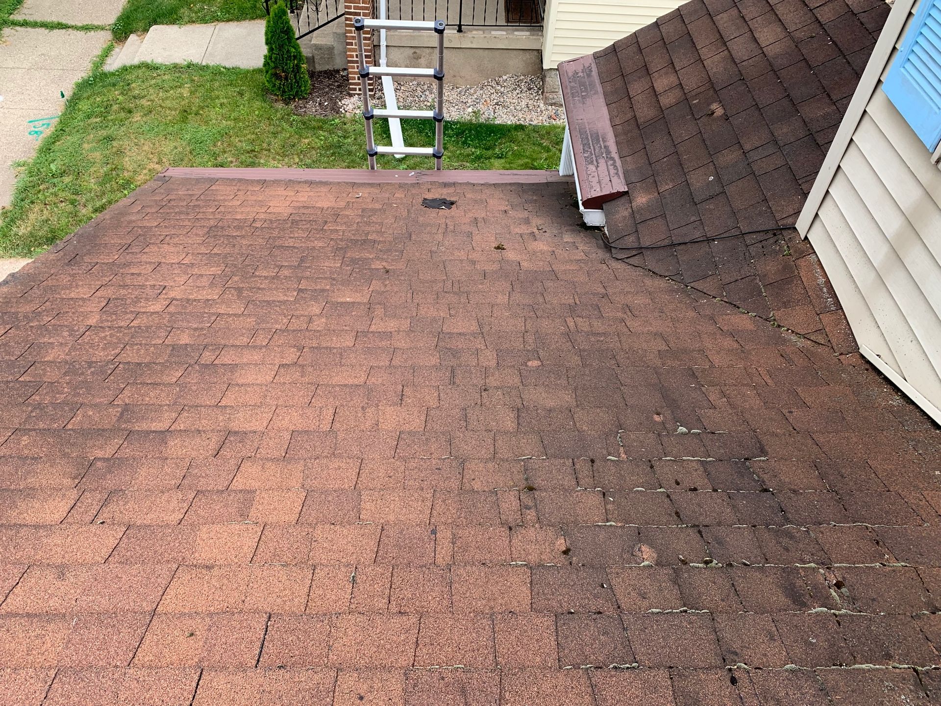 Weathered brown shingle roof with a small dormer and grassy yard below.