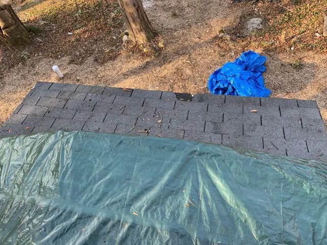 Blue tarp over a stack of gray cinder blocks on dirt ground with scattered debris